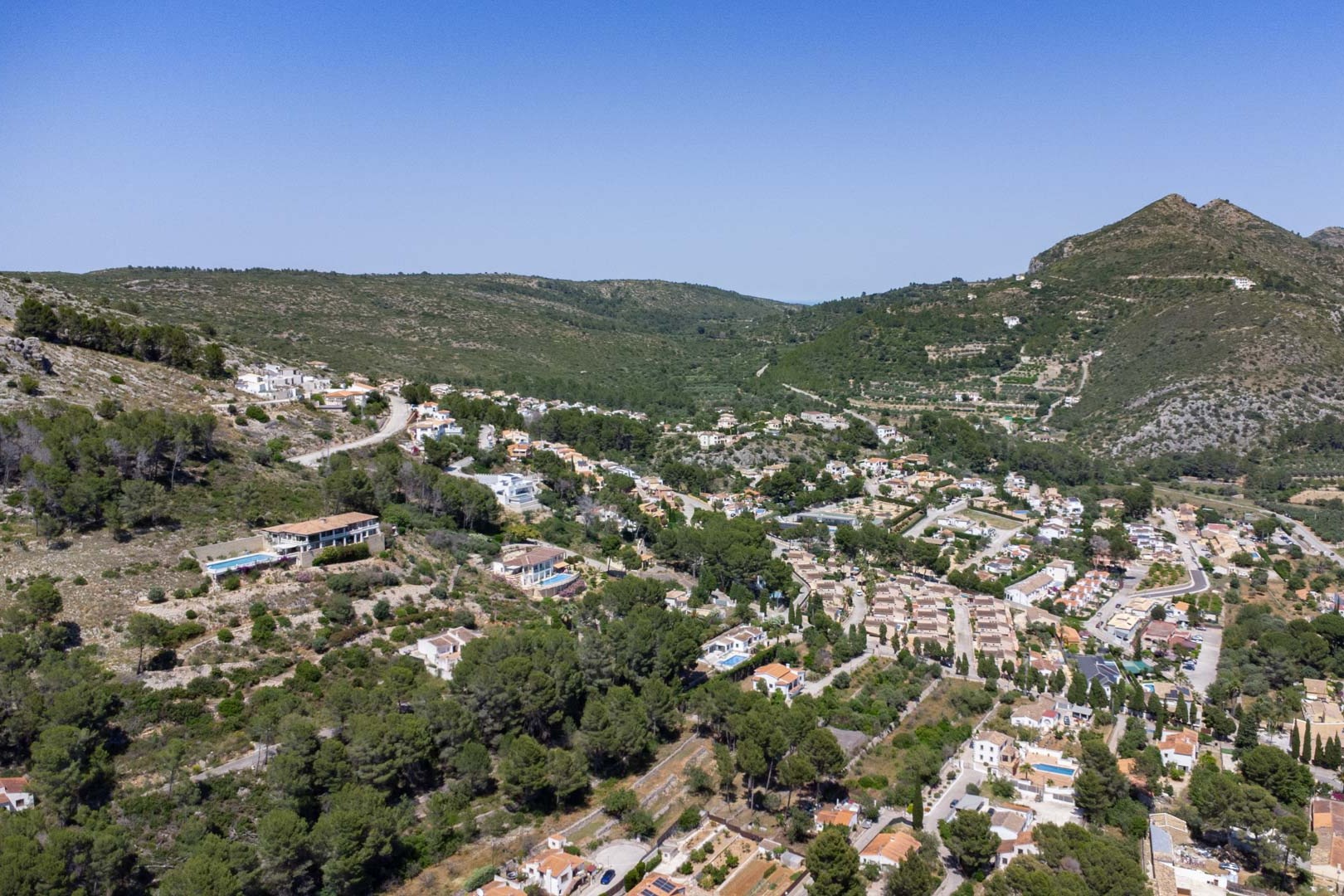 Panorama-Luftaufnahme der Wohnanlage VALL DE POP in Alcalalí, die die Integration der Villen in den Hang des Jalón-Tals inmitten mediterraner Vegetation zeigt.