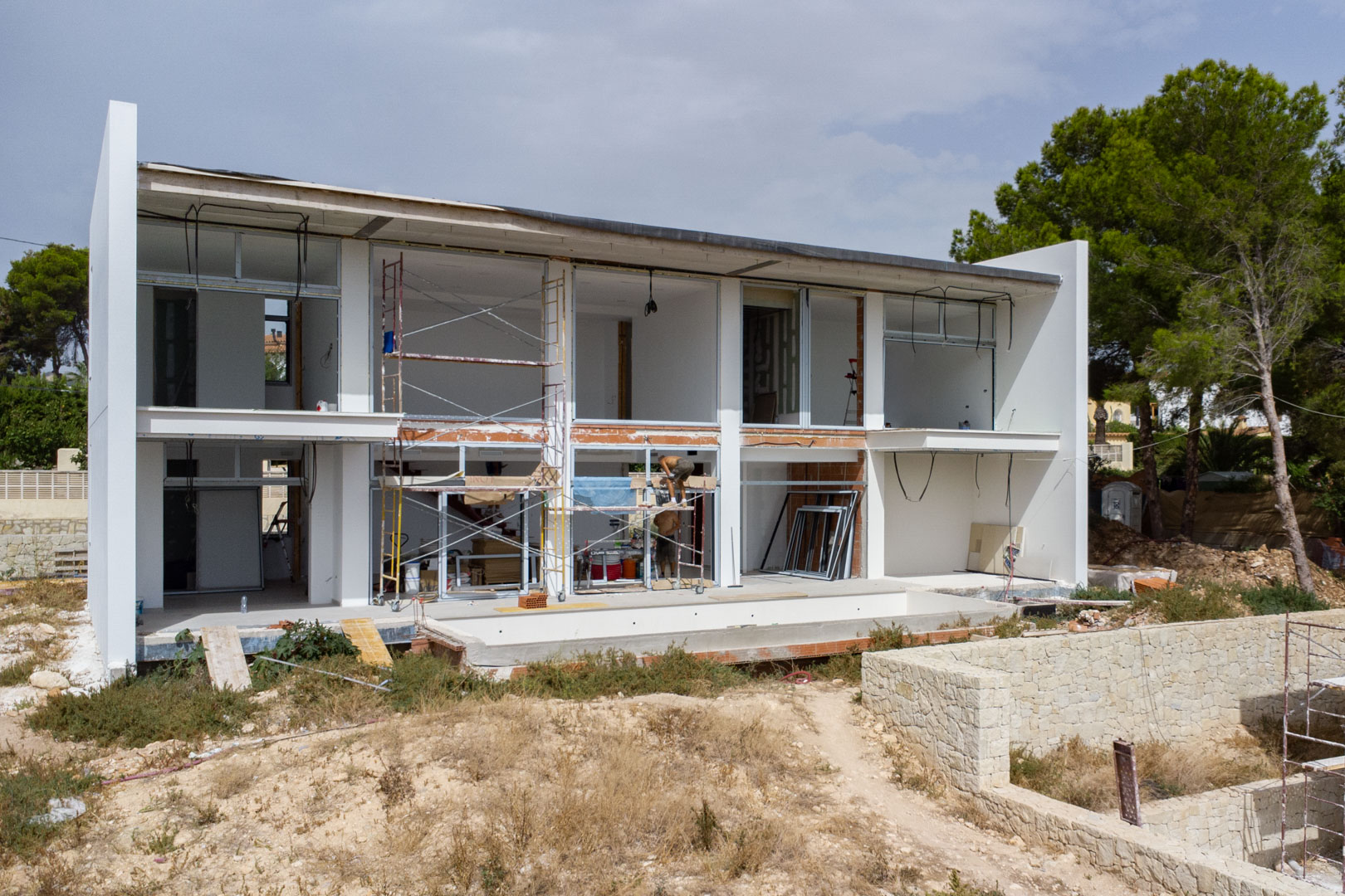 Außenansicht der Villa im Bau mit der zweistöckigen weißen Fassade, großen Fensterausschnitten und dem Bereich für das Schwimmbecken.
