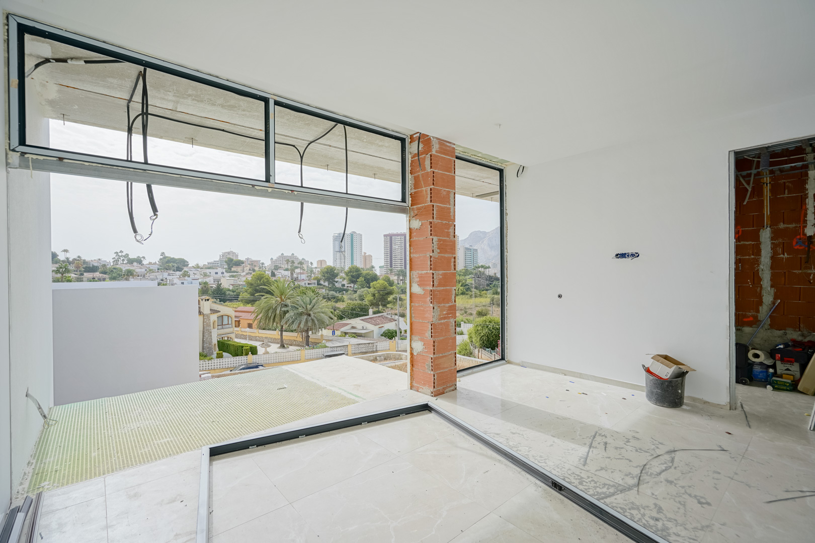 Innenansicht im Rohbau mit großen Fensterfronten, die einen weiten Blick auf den Peñón de Ifach und die Skyline von Calpe ermöglichen.