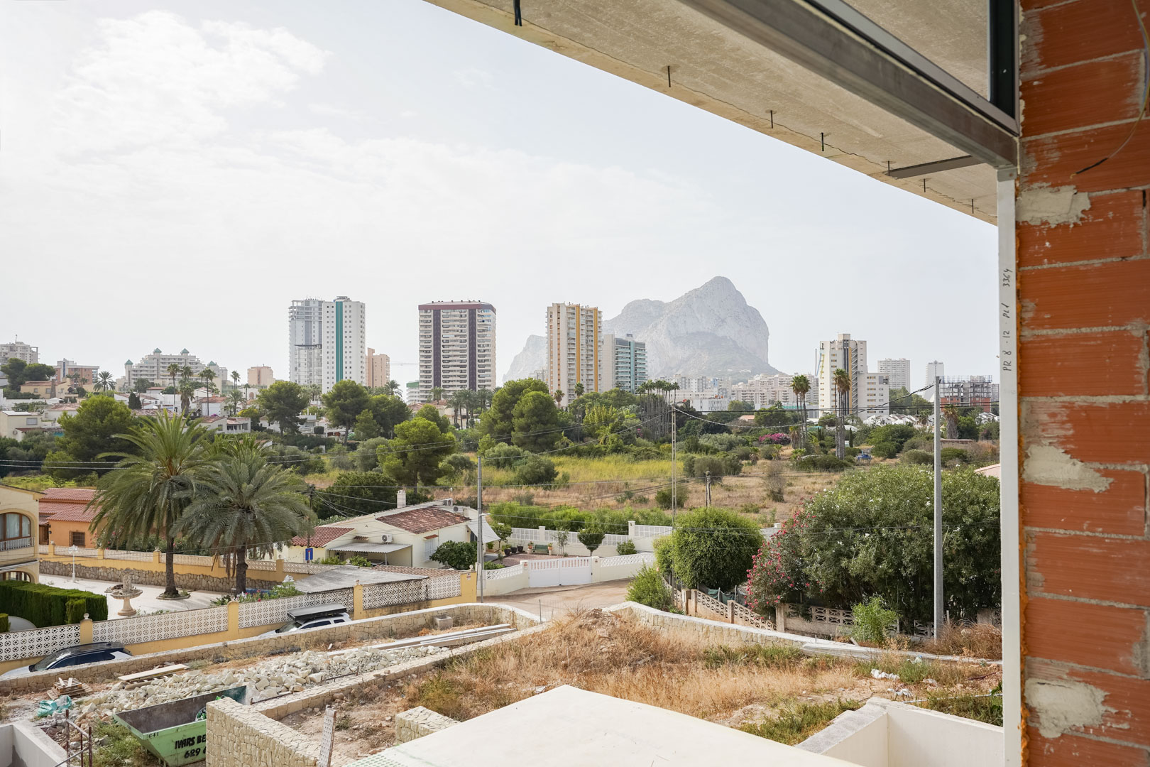 Panoramablick vom im Bau befindlichen Obergeschoss auf den Peñón de Ifach und die Skyline von Calpe, eingerahmt von Ziegelwänden und Betondecken.