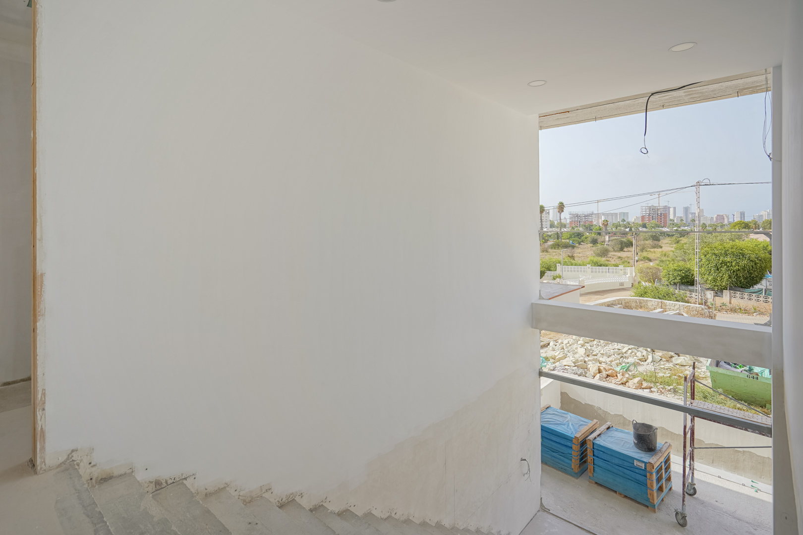 Blick vom Rohbau-Treppenhaus durch die große Fensteröffnung auf die Umgebung von Calpe und die umliegenden Baufortschritte.