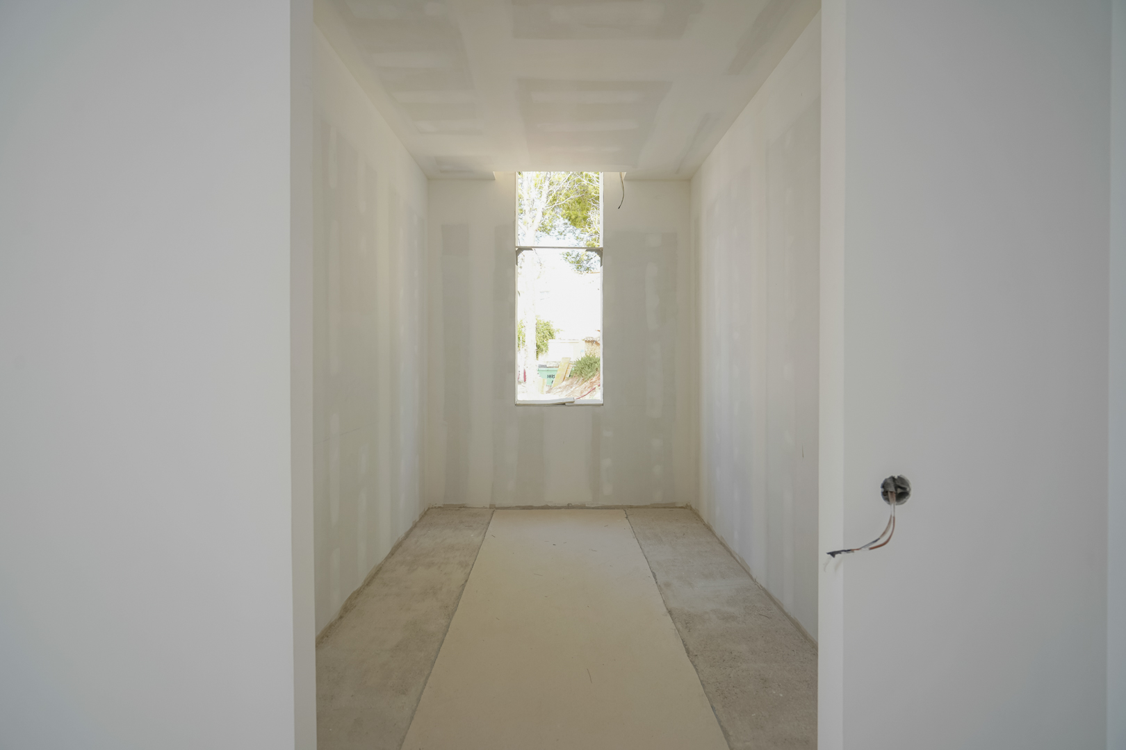 Innenansicht des begehbaren Kleiderschranks im Rohbau mit vertikalem Fenster für natürliches Licht und montierten Gipskartonplatten.