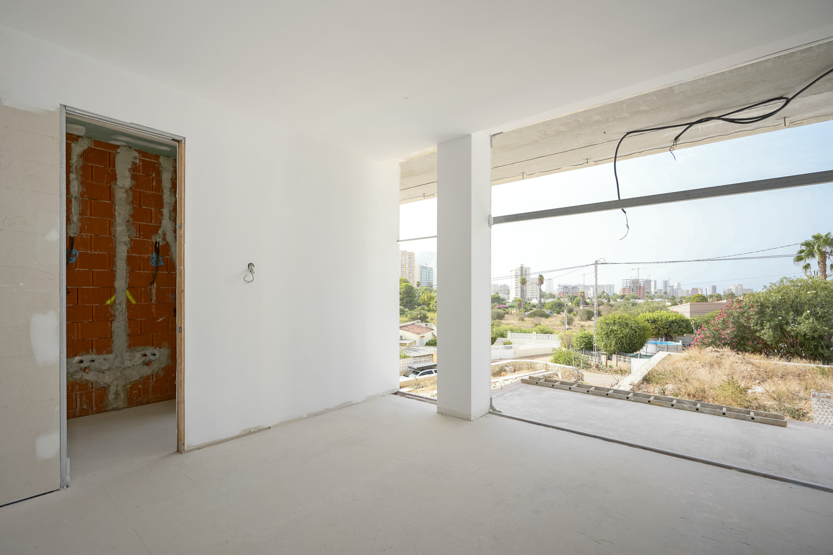 Innenansicht eines Raumes im Rohbau mit großen Fensteröffnungen und Blick auf die Skyline von Calpe sowie den markanten Peñón de Ifach.