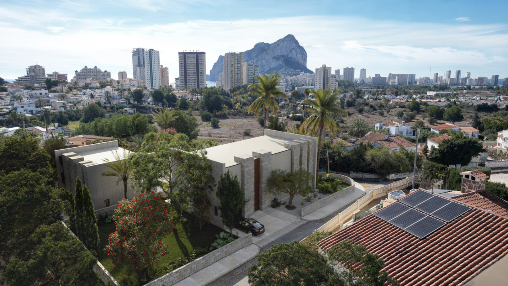 Luftaufnahme der modernen Villa mit Natursteinfassade und Gartenanlage, mit Blick auf den Peñón de Ifach und die Skyline von Calpe.