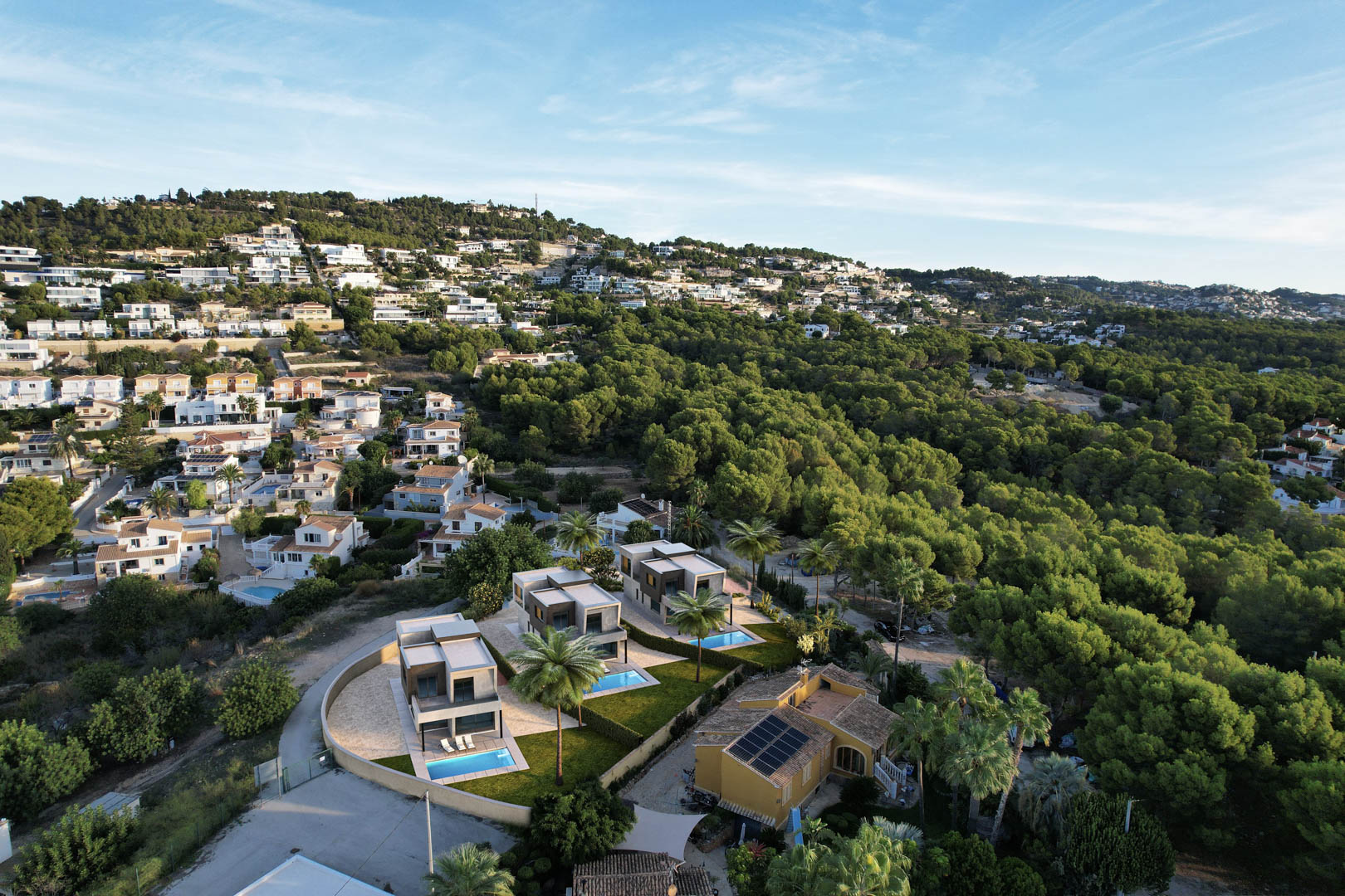 Luftaufnahme der drei modernen Villen mit privaten Pools und Gärten, gelegen an einem Hang direkt an einem Pinienwald in Calpe.