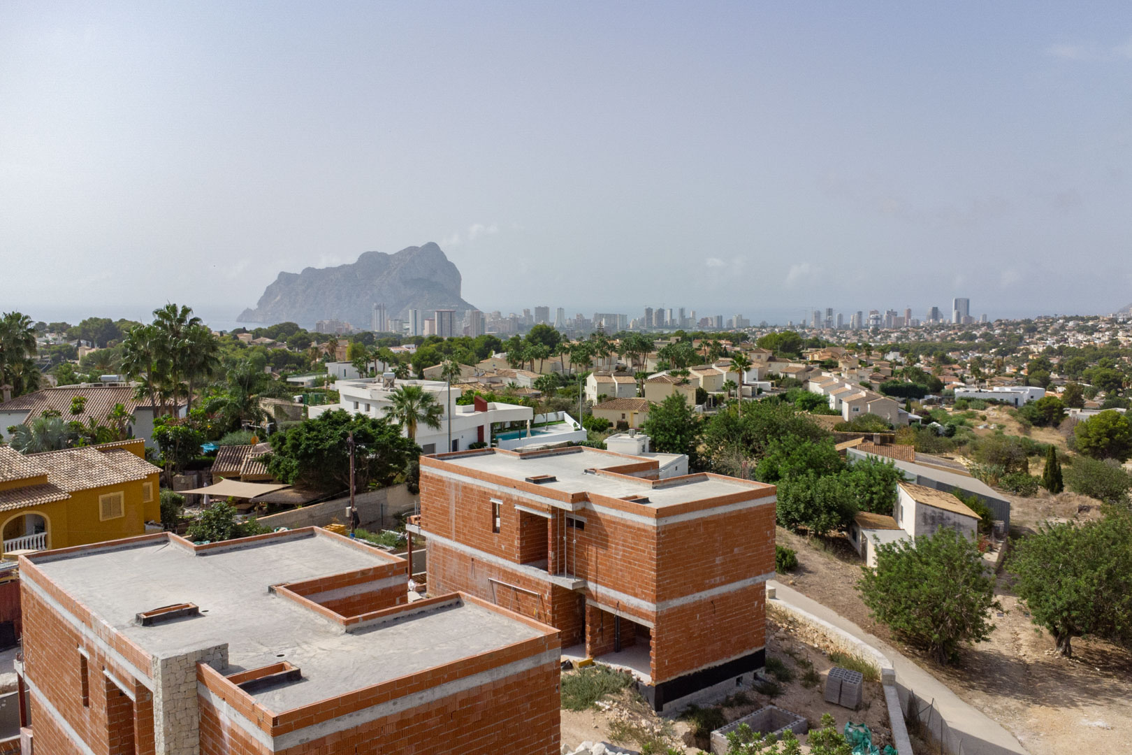 Luftaufnahme der im Bau befindlichen Villen im Rohbauzustand mit Panoramablick auf den Peñón de Ifach und die Skyline von Calpe.