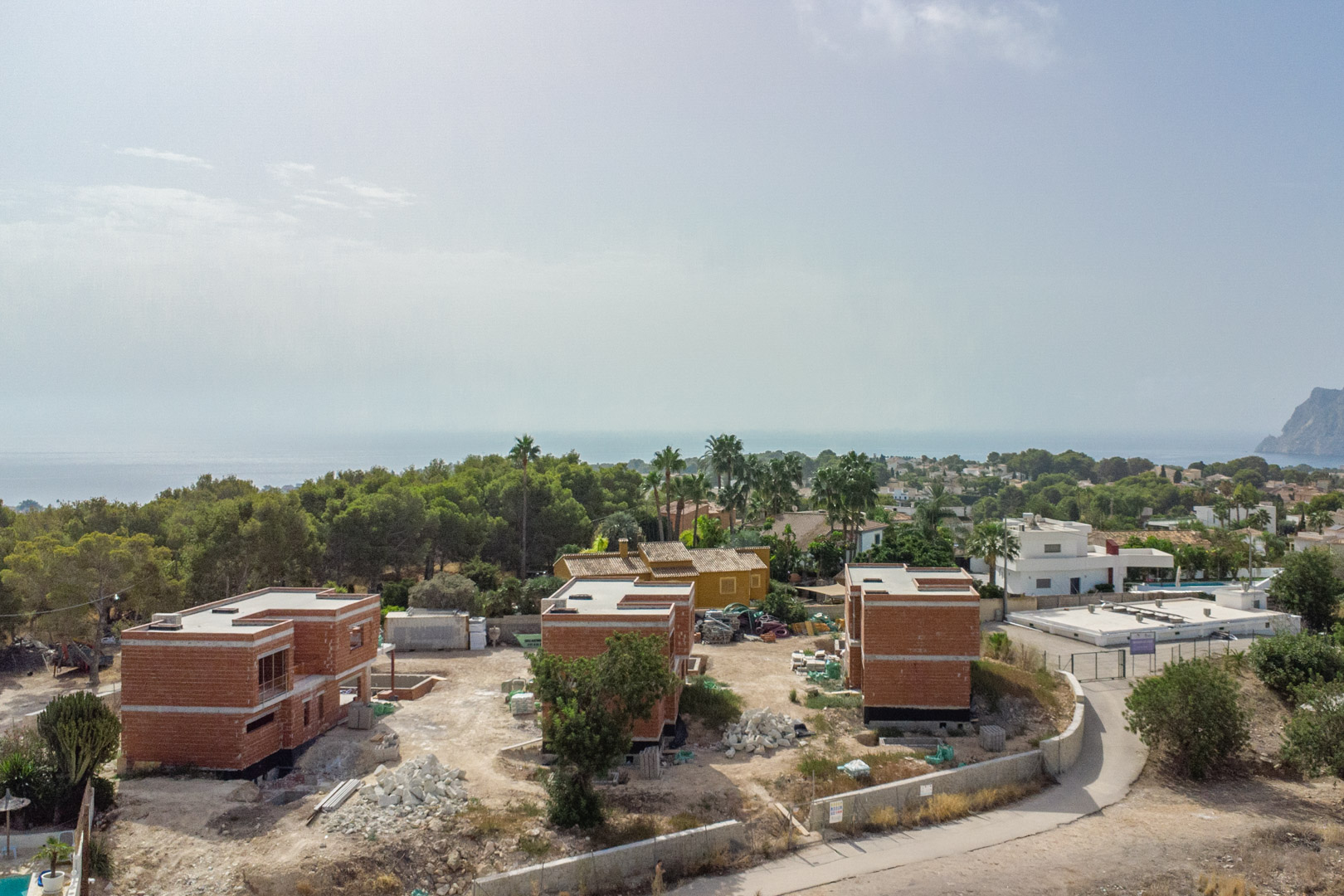 Luftaufnahme des Baufortschritts der drei Luxusvillen mit Blick auf die Rohbaustrukturen, das Mittelmeer und den markanten Peñón de Ifach im Hintergrund.