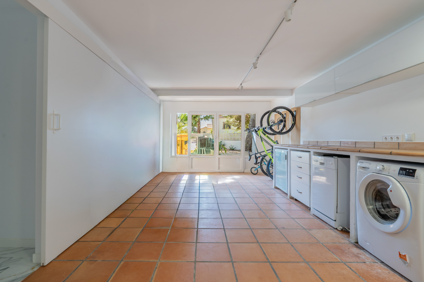 Ausgebauter Garagenbereich mit Terrakottaboden, Waschküche inklusive Elektrogeräten, Stauraum und direktem Zugang zum mediterranen Garten.