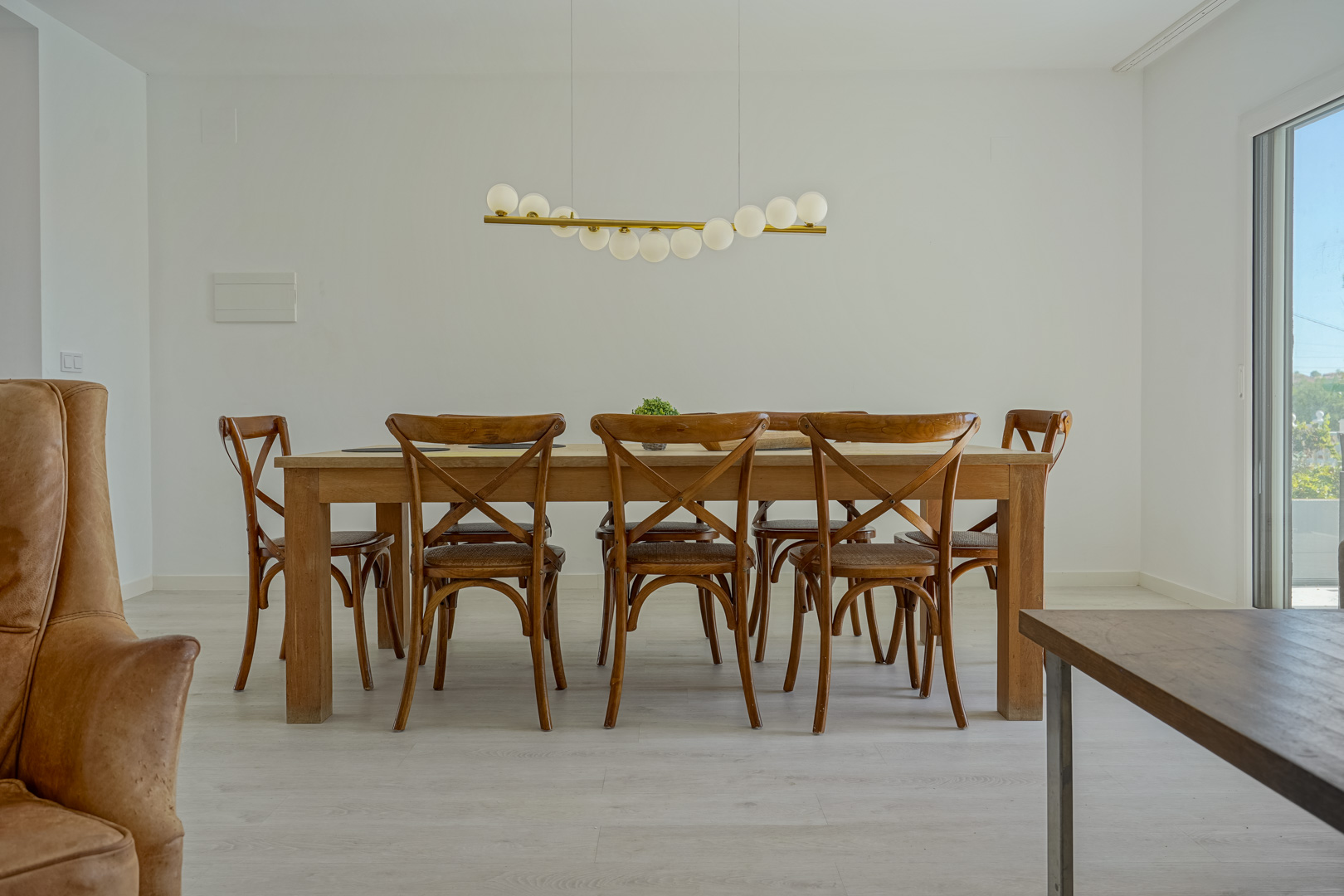 Essbereich mit massivem Holztisch, Cross-Back-Stühlen und einer modernen Pendelleuchte über hellem Bodenbelag in Holzoptik.