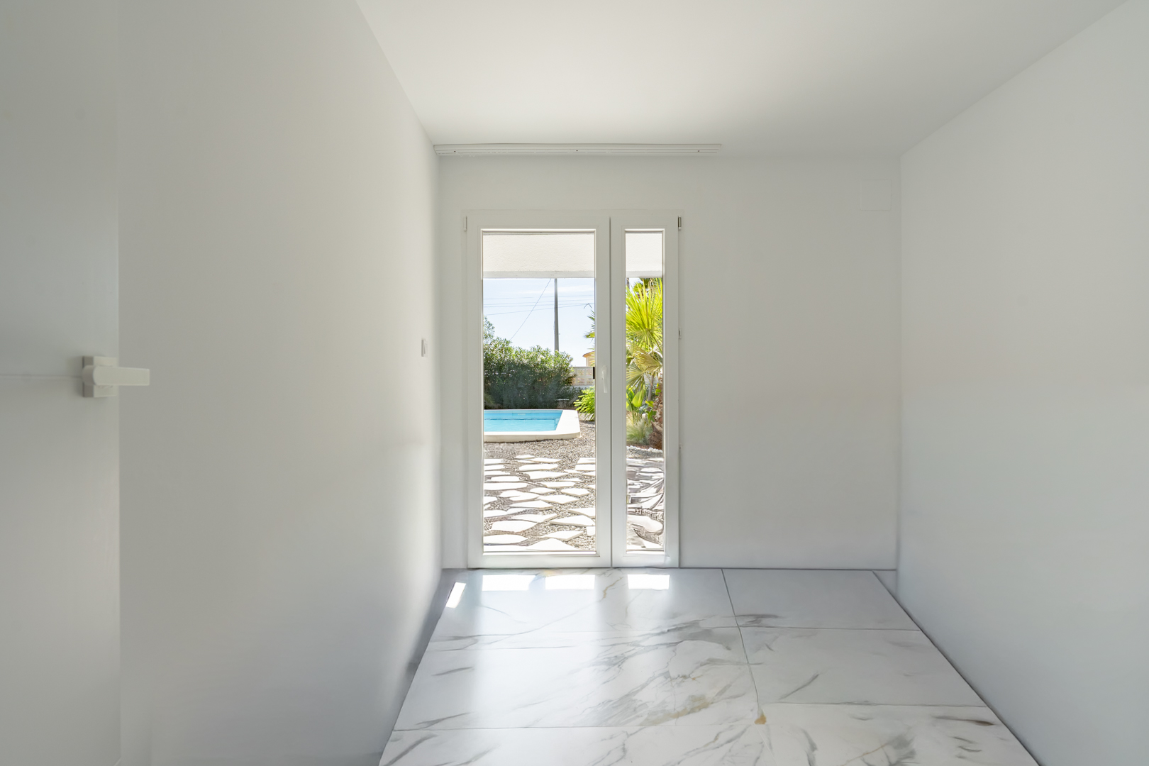 Heller Raum mit Feinsteinzeugboden in Marmoroptik und direktem Zugang zur Poolterrasse durch eine Glastür.