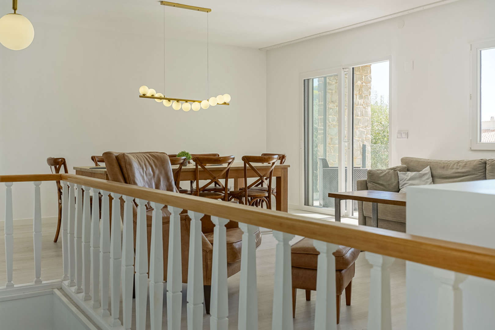 Heller Wohn-Essbereich mit klassischem Geländer, Holztisch, Designer-Pendelleuchte und direktem Zugang zur Terrasse durch große Glasschiebetüren.