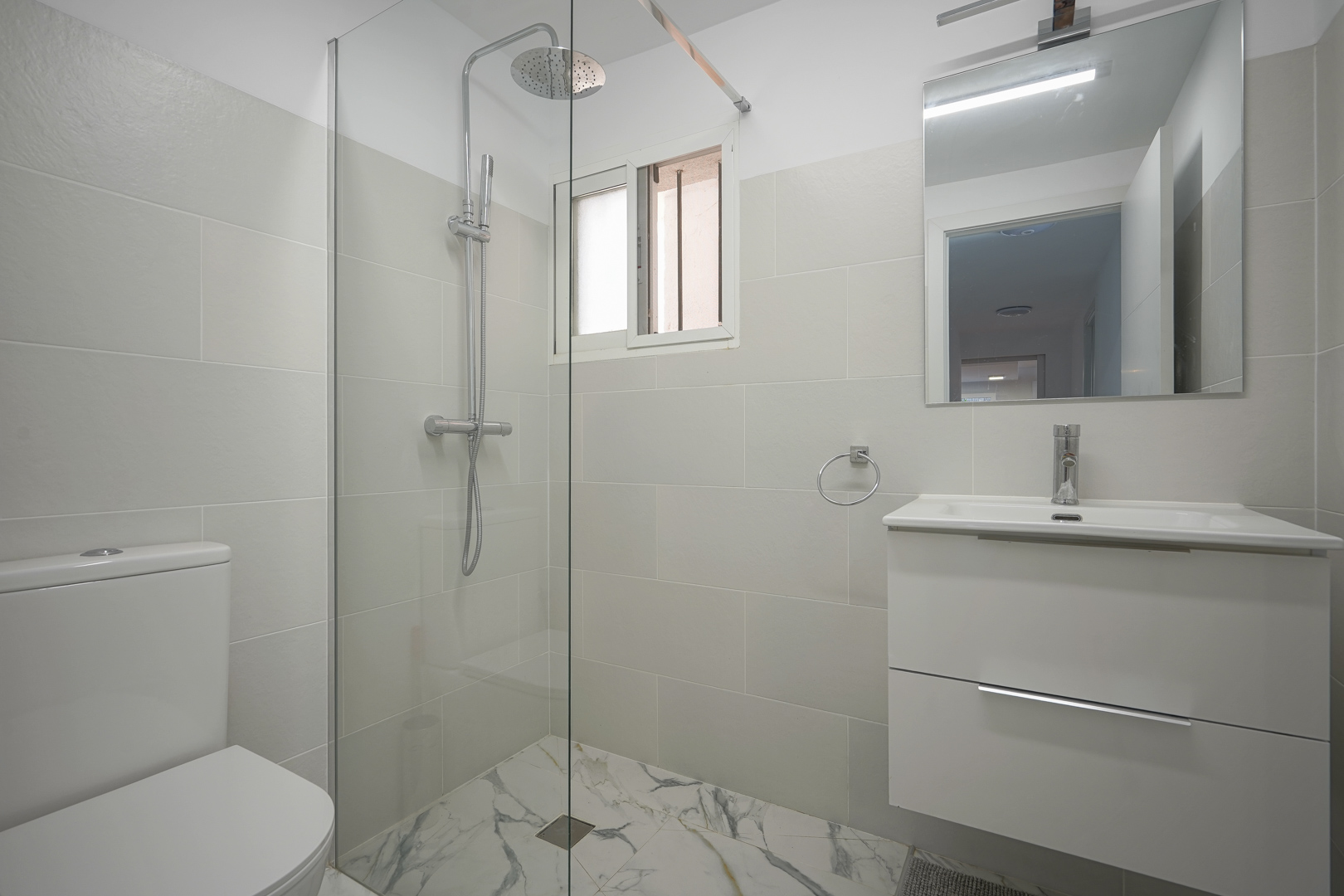 Modernes Badezimmer mit begehbarer Dusche, Glastrennwand, weißem Waschtisch und Bodenfliesen in Marmoroptik.