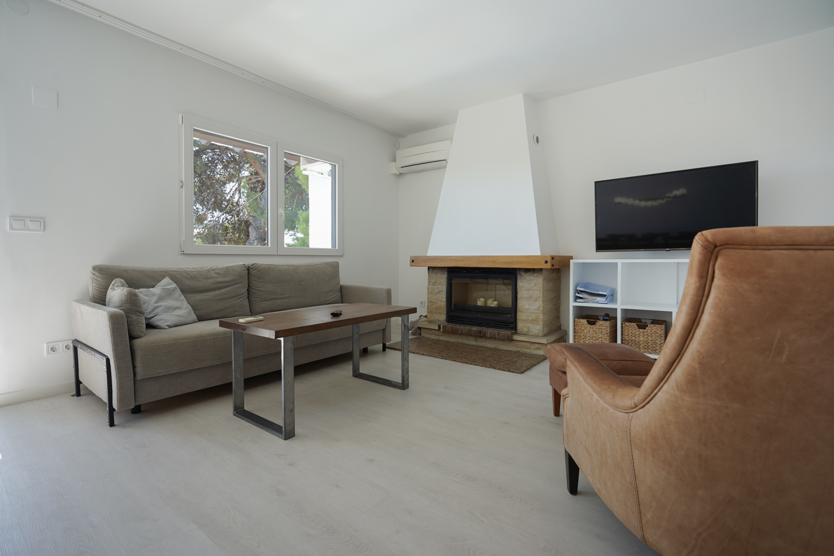 Modernes Wohnzimmer mit Stein-Kamin, Holzsims, Ledersessel und grauem Sofa. Ausgestattet mit Klimaanlage und doppelt verglasten Fenstern für helles Tageslicht.