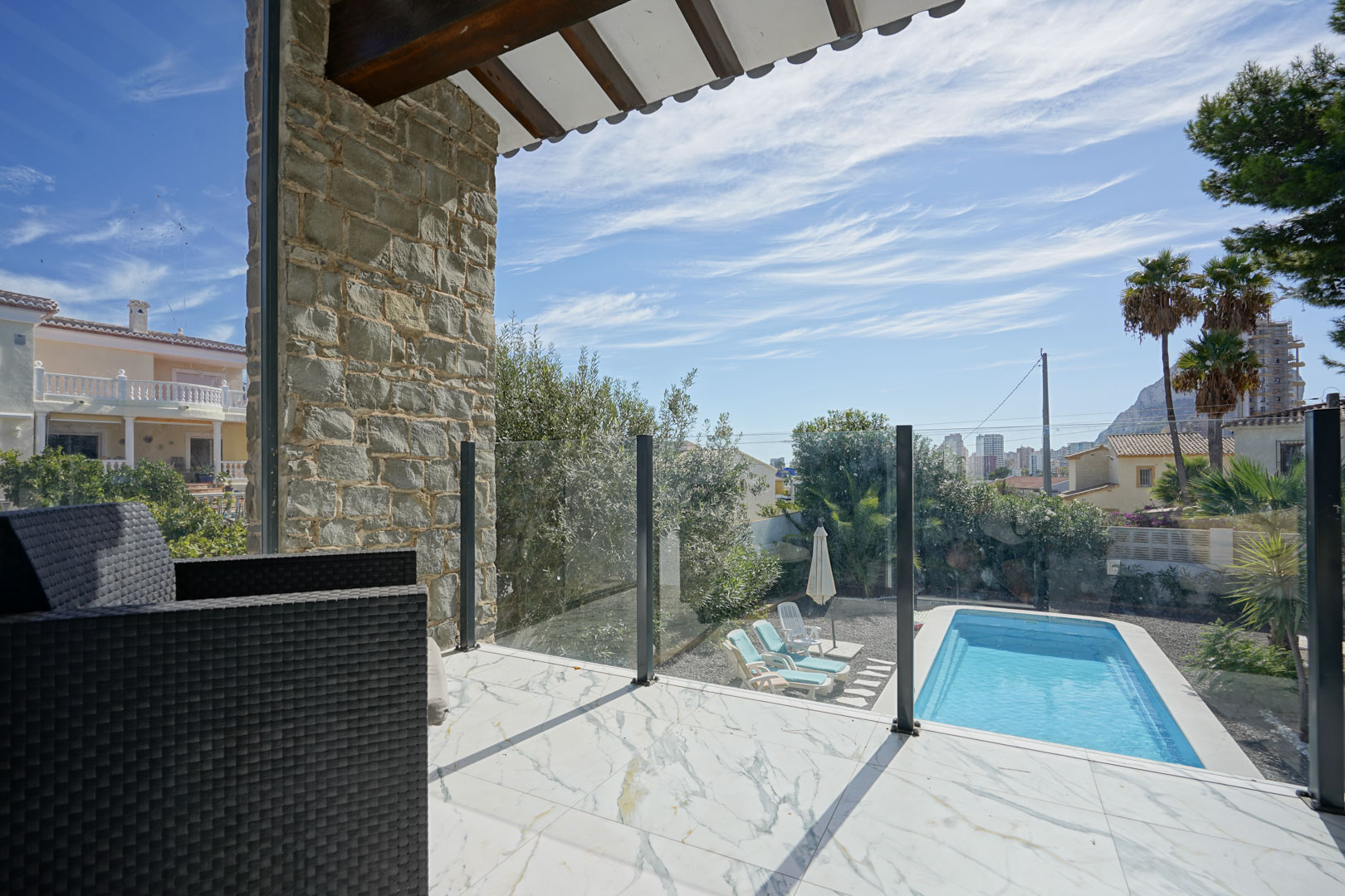 Obere Terrasse mit Marmorfliesen, Glasgeländer und Blick auf den privaten Pool, den Garten und den Peñón de Ifach in der Ferne.