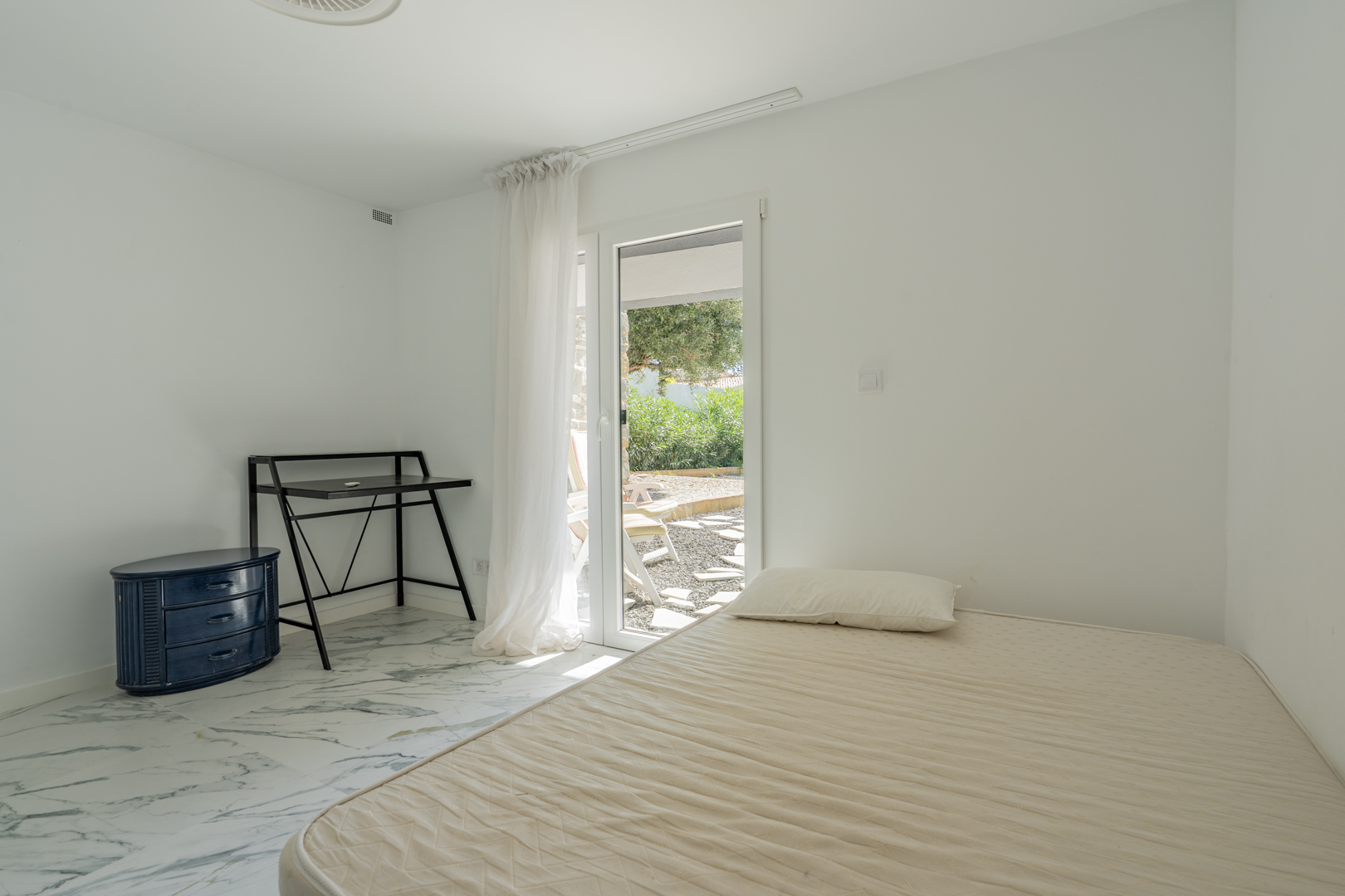 Schlafzimmer mit Marmorboden und direktem Zugang zur Gartenterrasse. Ausgestattet mit einem Schreibtisch und einer blauen Kommode.