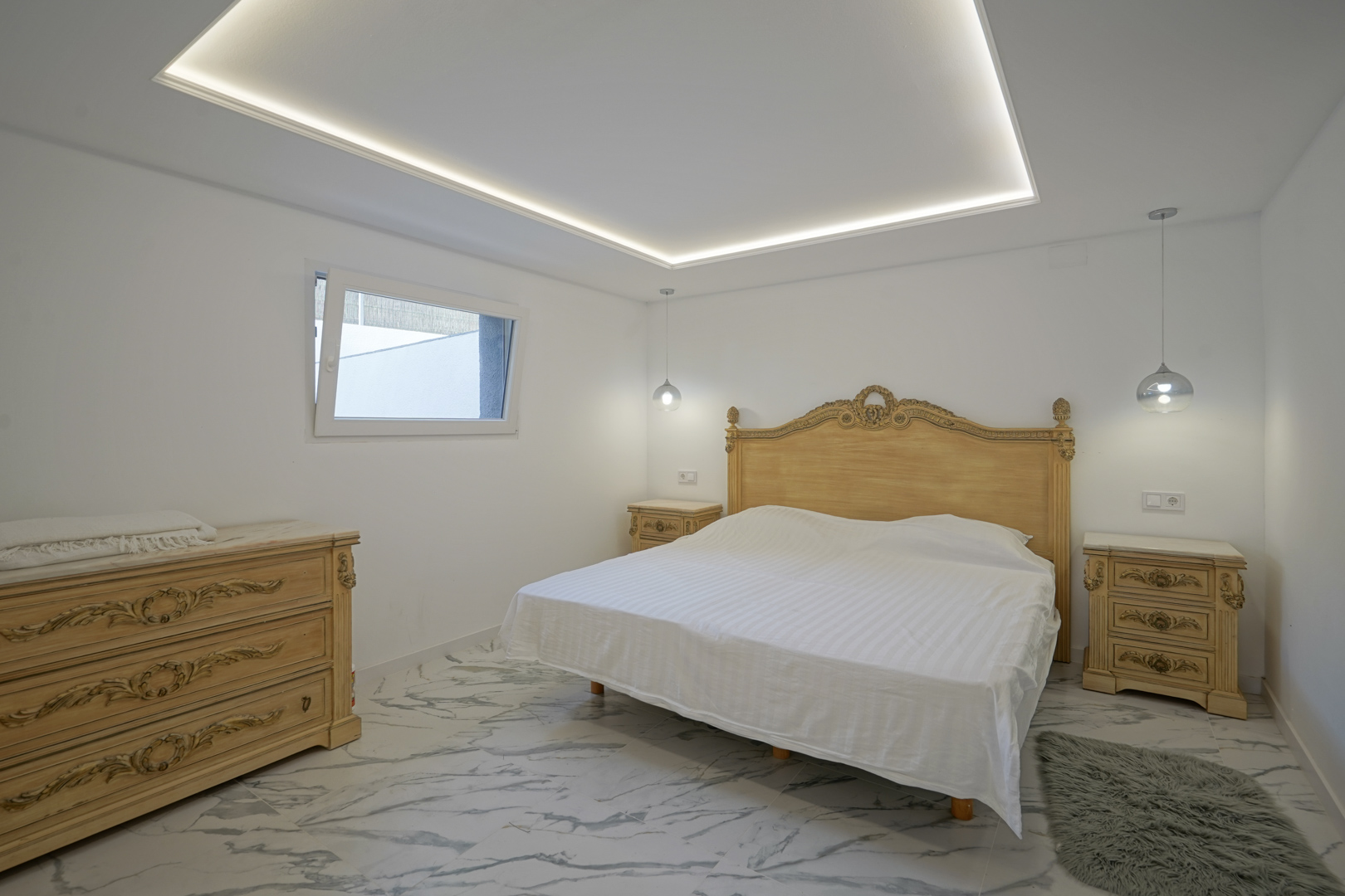 Schlafzimmer mit verzierten klassischen Möbeln, Marmoreffekt-Fliesenboden und abgehängter Decke mit integrierter LED-Umfeldbeleuchtung.