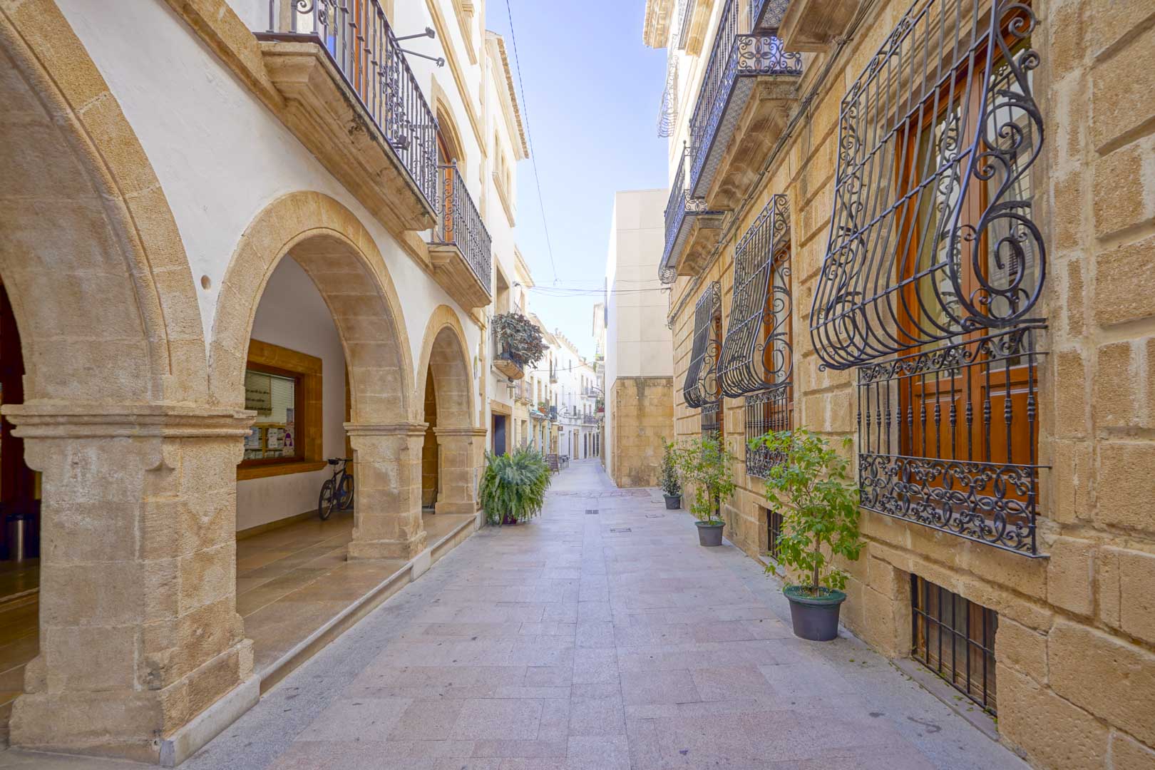 Fußgängerzone in der Altstadt von Jávea mit traditionellen Tosca-Steinbögen, schmiedeeisernen Gittern und mediterraner Architektur.