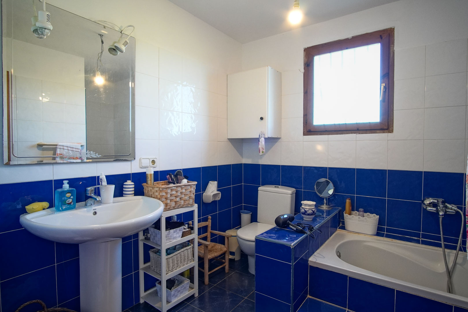 Badezimmer mit blau-weißen Fliesen, Standwaschbecken, Einbaubadewanne und einem Holzfenster für natürliches Licht.