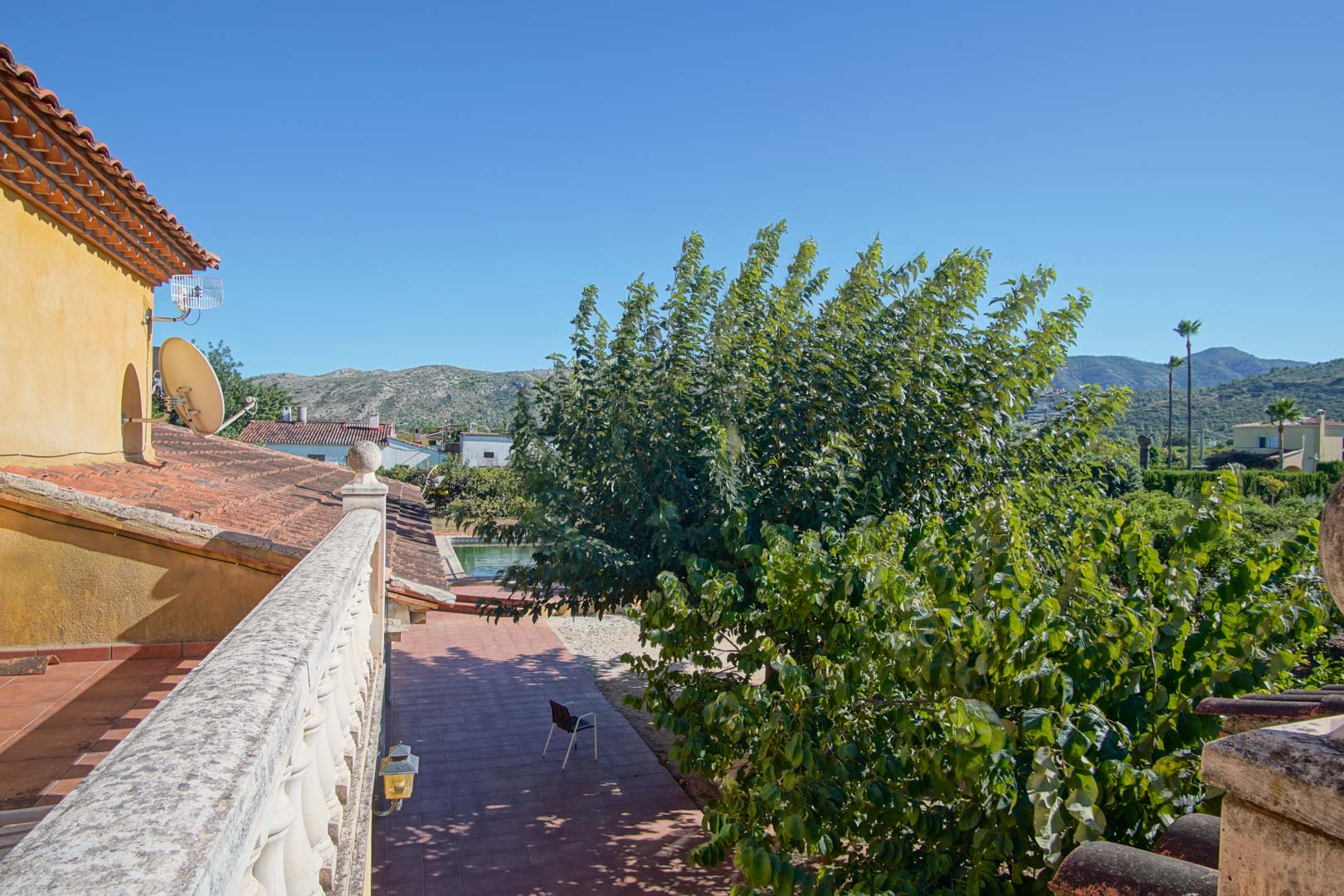 Blick von der oberen Terrasse mit Steinbalustrade auf den gefliesten Hof, den Pool und die Vegetation vor dem Panorama der Segaria-Berge.