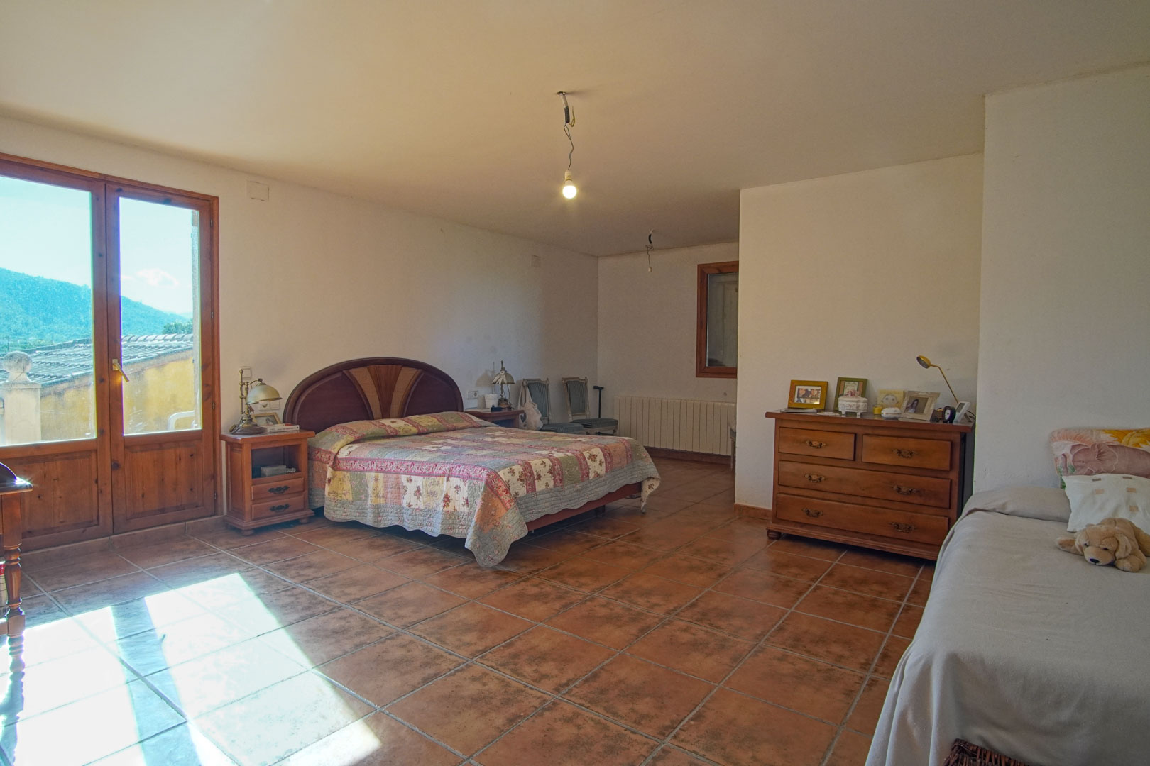 Großzügiges Schlafzimmer mit rustikalem Terrakottaboden, klassischen Holzmöbeln und Glastür mit Blick auf die umliegende Berglandschaft.