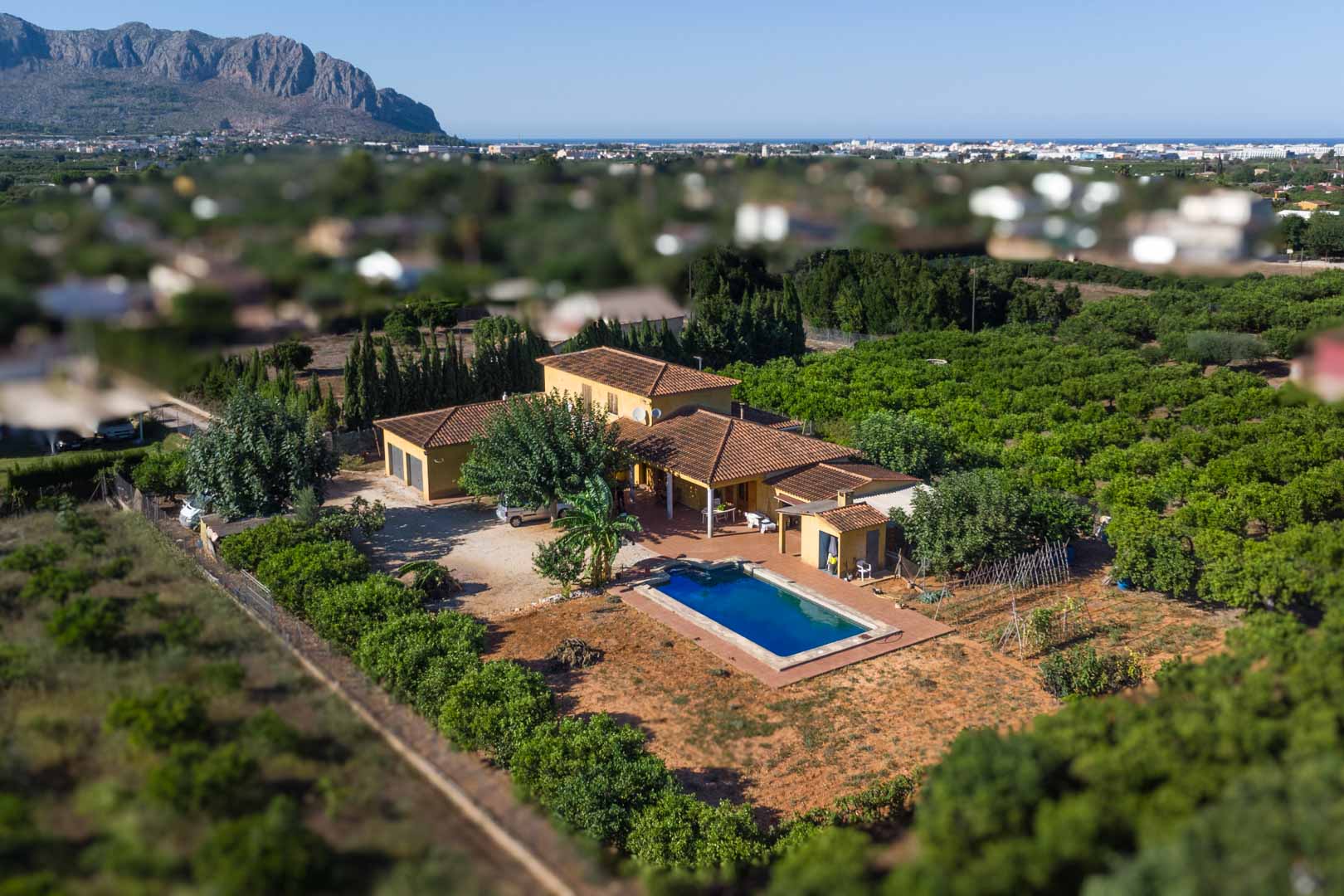 Luftaufnahme der Villa mit rechteckigem Pool und Obstgärten, im Hintergrund der Berg Segaria und die mediterrane Küstenlinie am Horizont.