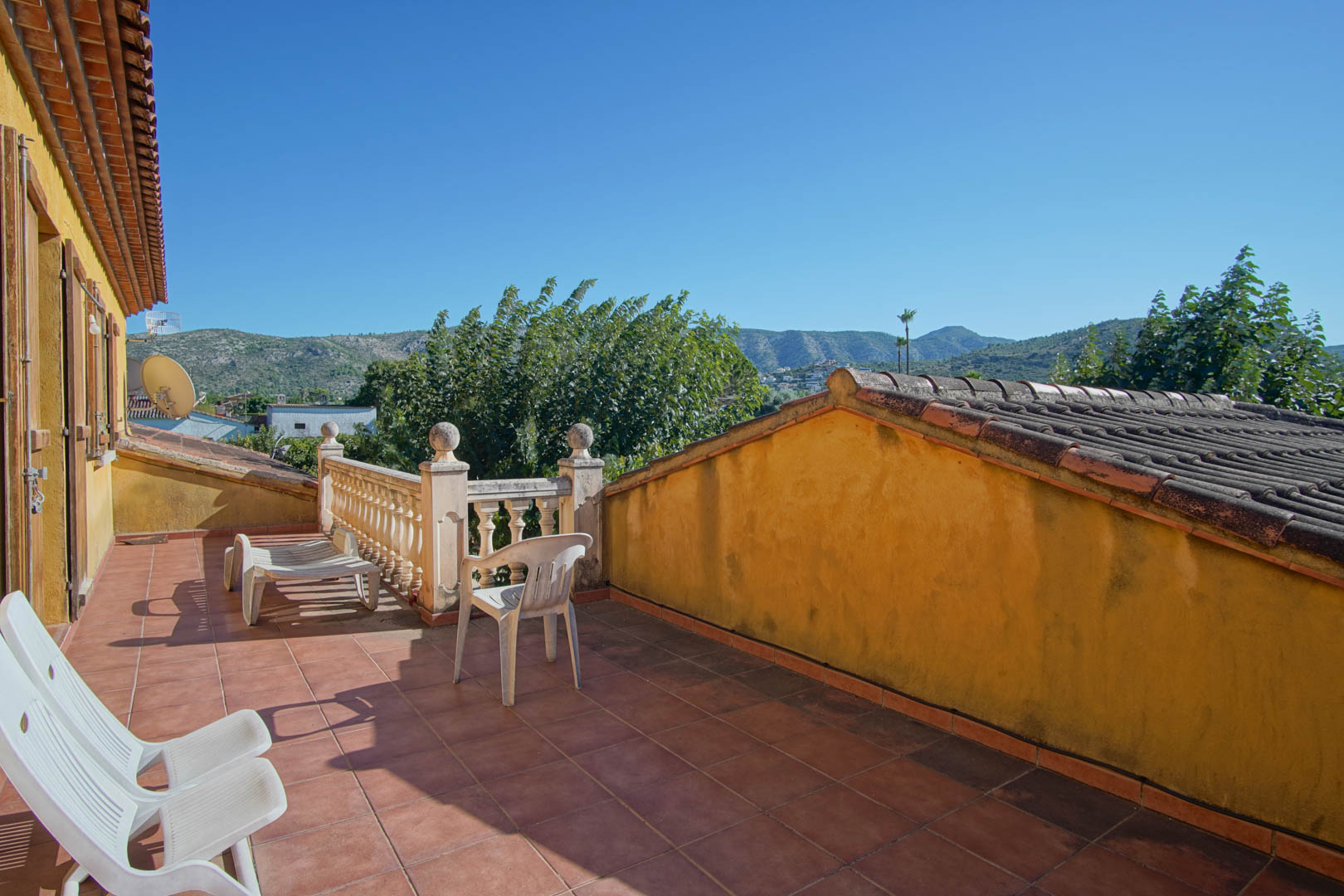 Obere Terrasse mit rustikalen Terrakottafliesen und Steinbalustrade, die einen weiten Blick auf das Segaria-Gebirge und die grüne Landschaft bietet.