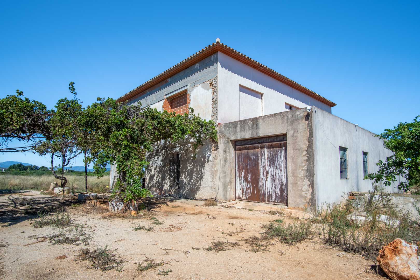 Außenansicht des Landhauses in Renovierung mit gefestigter Struktur, flachem Grundstück und weitem Blick auf die umliegenden Berge von Dénia.