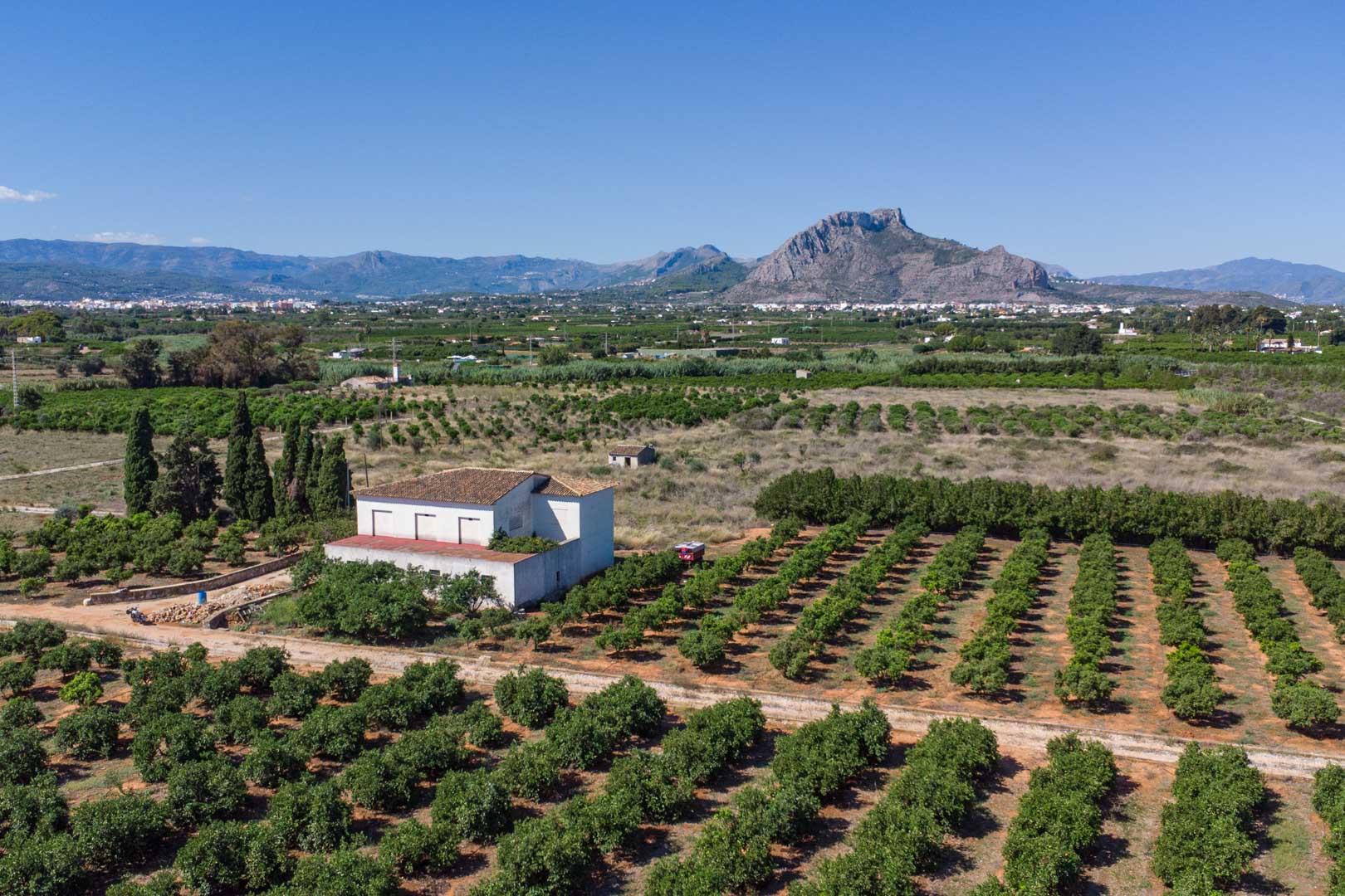 Luftaufnahme des Landhauses inmitten weitläufiger Zitrusplantagen mit freiem Blick auf die Berge und die flache mediterrane Landschaft.