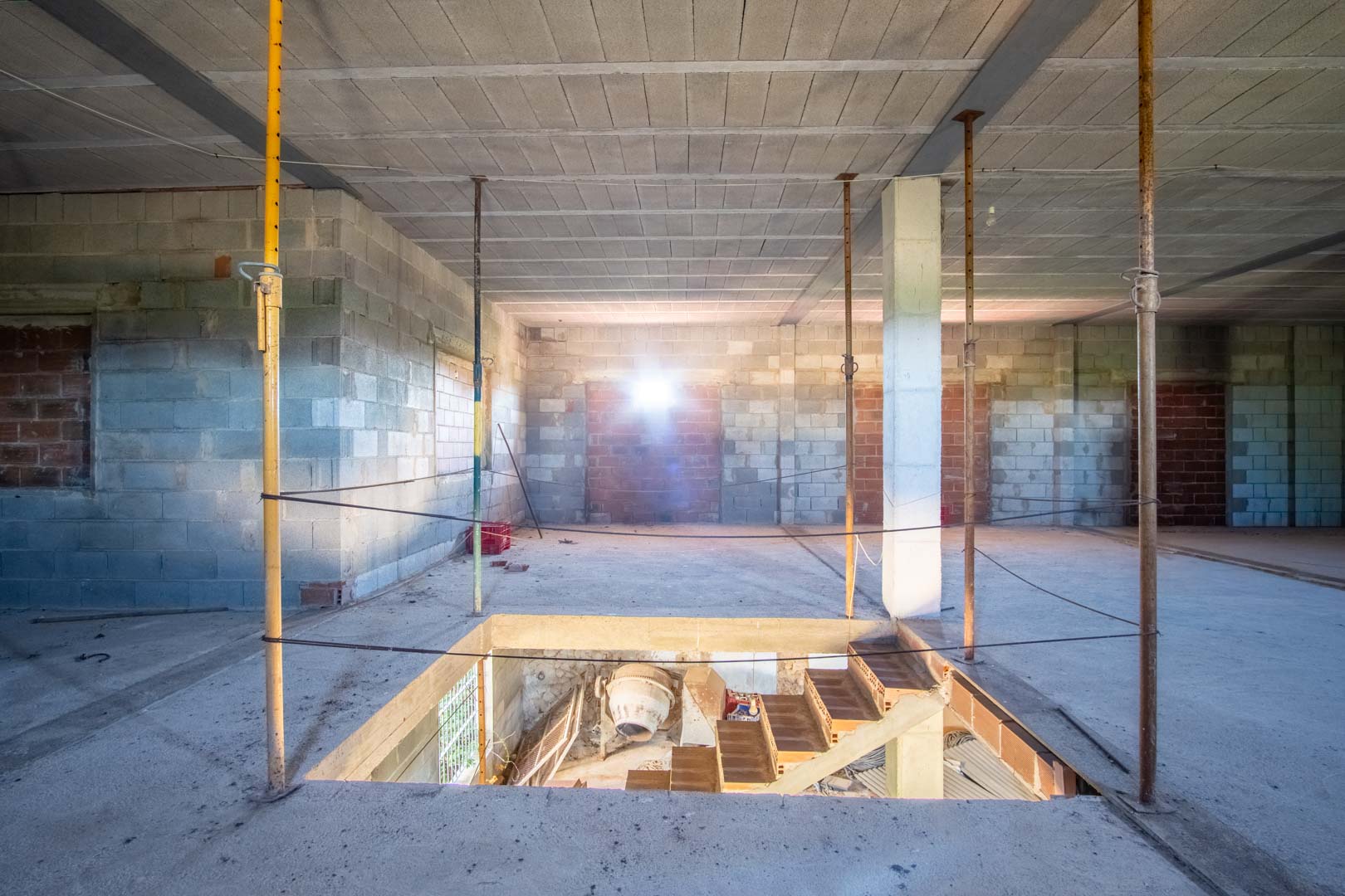 Offener Innenraum im Rohbau mit Betonblockwänden, Stahlträgern und einer Deckenöffnung für die Treppe zum Untergeschoss.