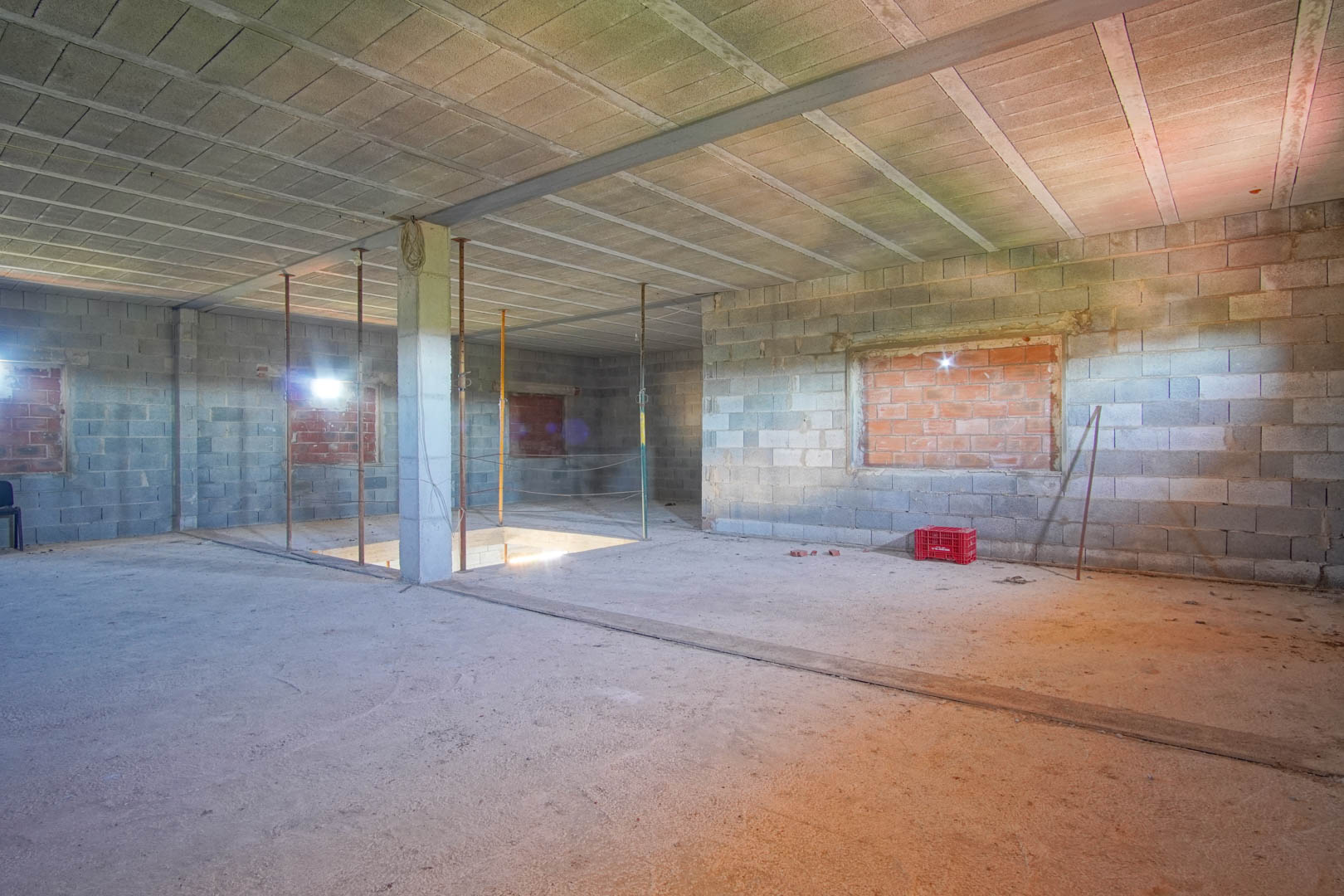 Offener Innenraum im Rohbauzustand mit Betonblockwänden, Stahlträgern und Treppenaussparung, bereit für die individuelle Raumaufteilung.