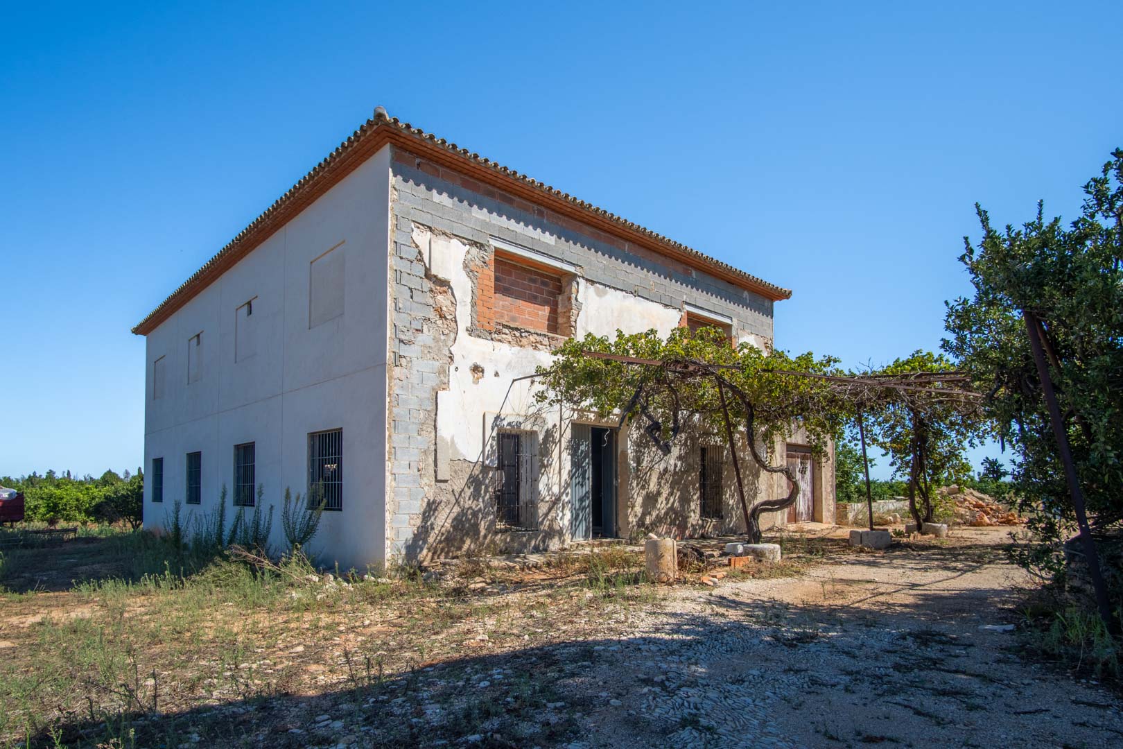 Zweistöckiges Landhaus in der Renovierungsphase mit traditionellem Ziegeldach, natürlicher Weinlaube und einer soliden Grundstruktur auf ebenem Grundstück.