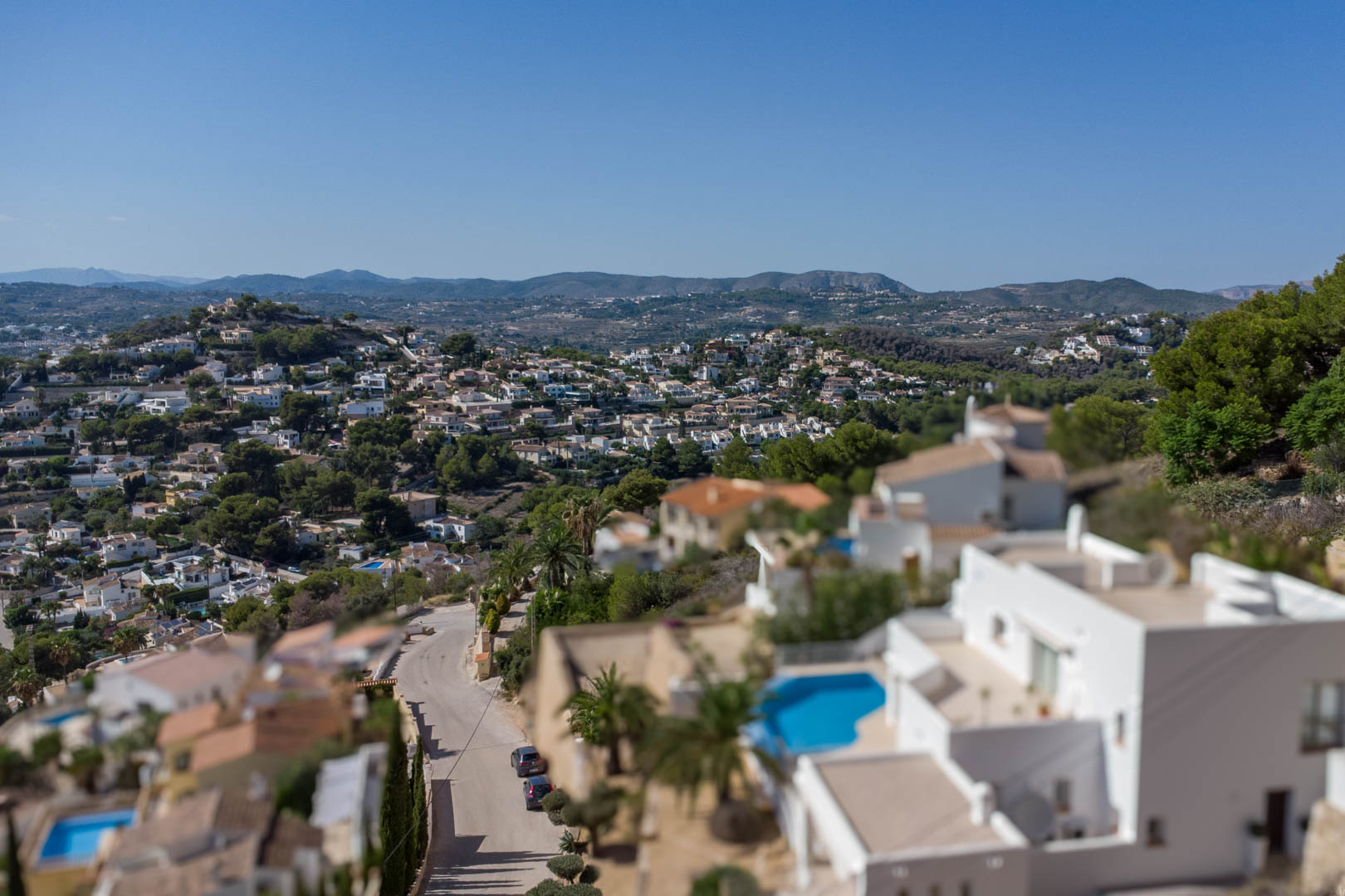 Erhöhter Panoramablick auf das Wohnviertel El Portet mit weißen Villen, privaten Pools und der hügeligen Landschaft unter strahlend blauem Himmel.