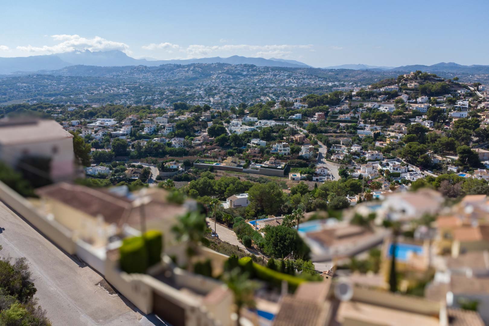 Erhöhter Panoramablick über das Wohngebiet El Portet mit mediterraner Vegetation und fernen Bergketten unter klarem blauem Himmel.