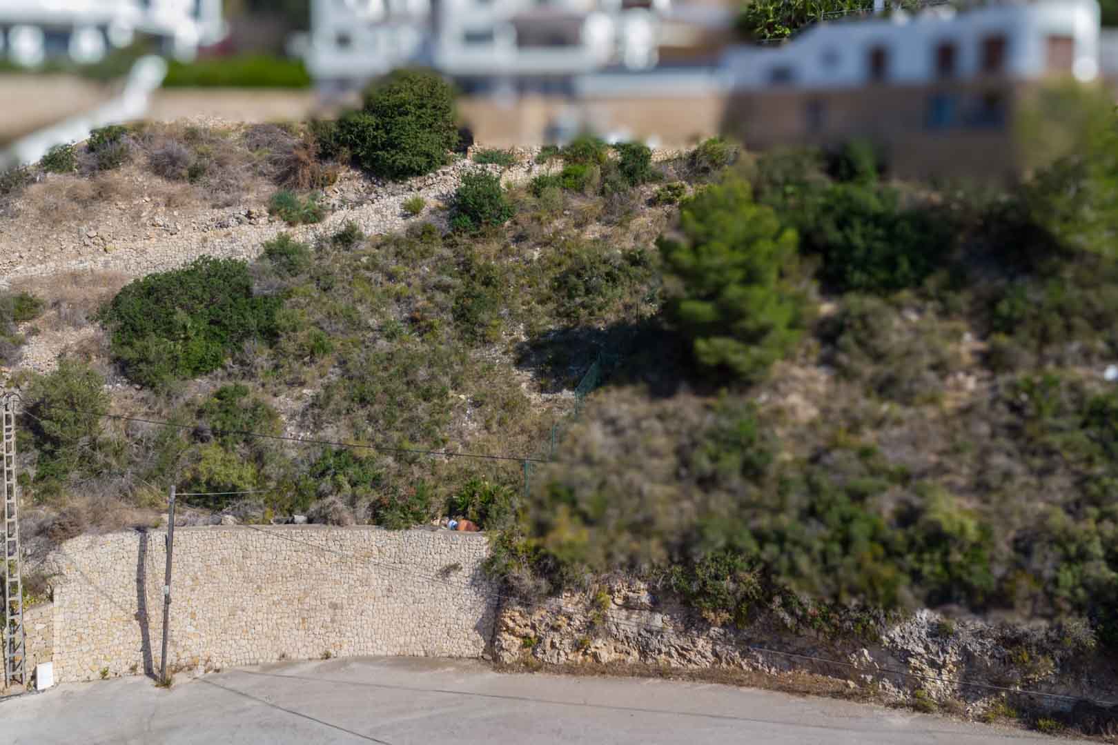 Erhöhtes Baugrundstück mit Natursteinstützmauern und mediterraner Bepflanzung in einem etablierten Wohngebiet von El Portet.