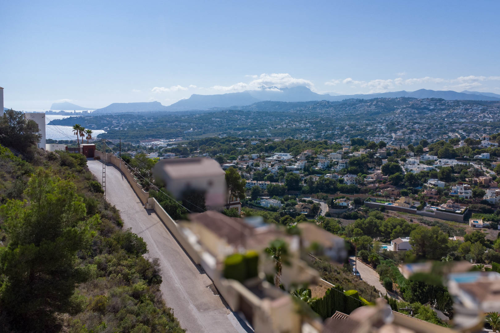 Panoramablick vom erhöhten Grundstück in El Portet über das Wohngebiet, die Küste von Moraira und die fernen Bergketten bei klarem Himmel.