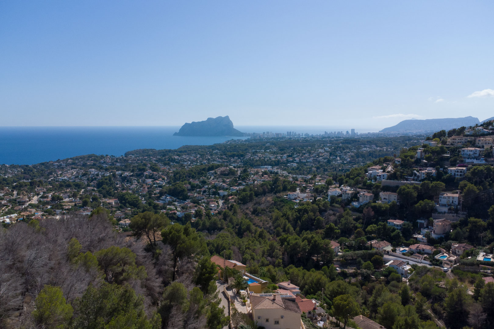 Erhöhter Panoramablick auf das Mittelmeer und den Peñón de Ifach, eingebettet in die grüne Küstenlandschaft und Wohngebiete der Costa Blanca.