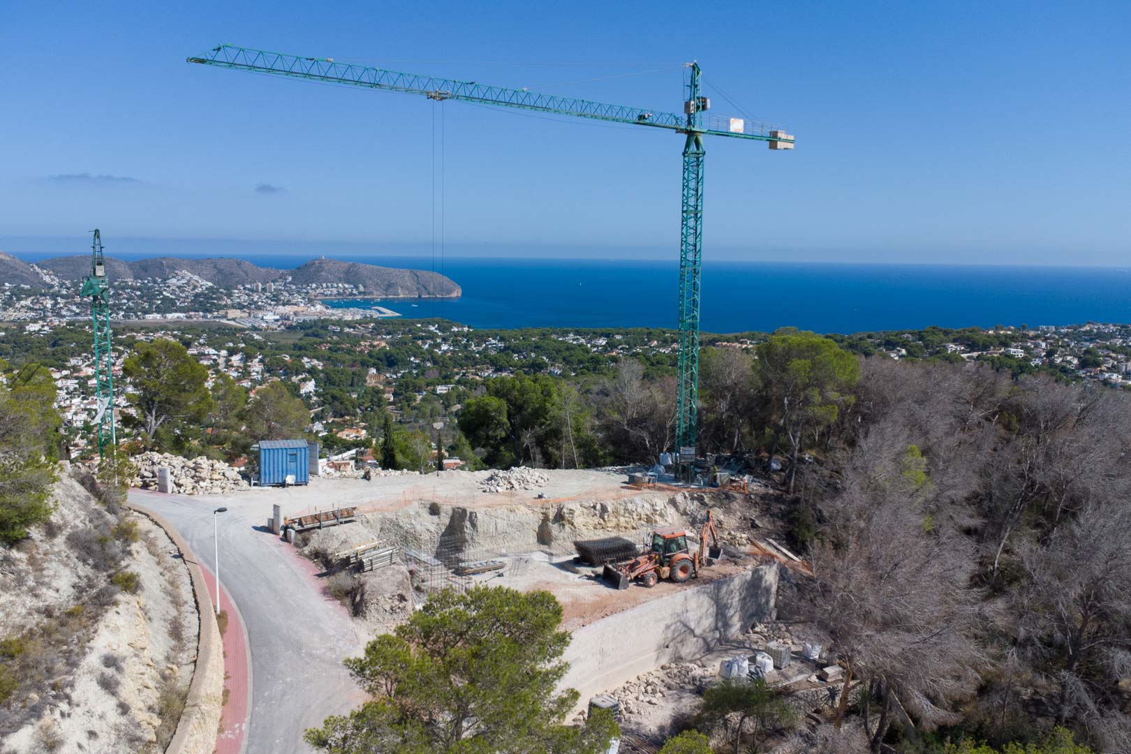 Luftaufnahme des Baugrundstücks in der Erschließungsphase mit Baukran und Panoramablick auf das Mittelmeer und die Küstenlandschaft von Moraira.
