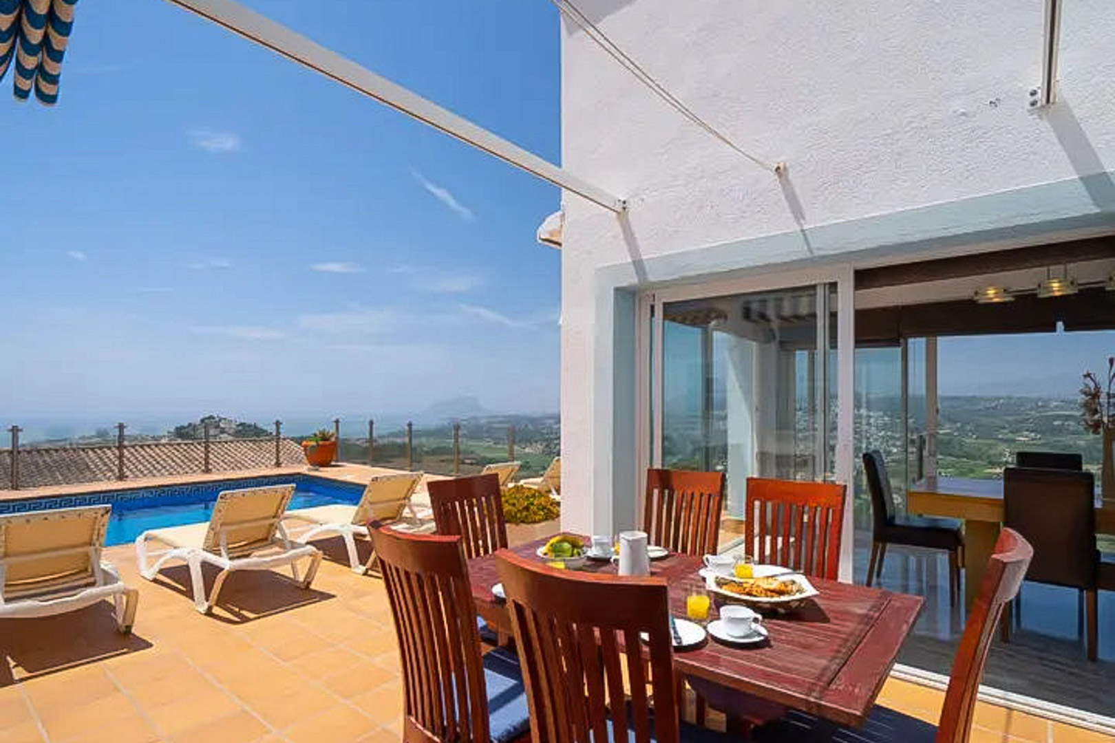 Außen-Terrasse mit Holz-Essgruppe, privatem Pool mit Mosaikrand und Panoramablick auf das Mittelmeer und die Küstenlandschaft von Moraira.