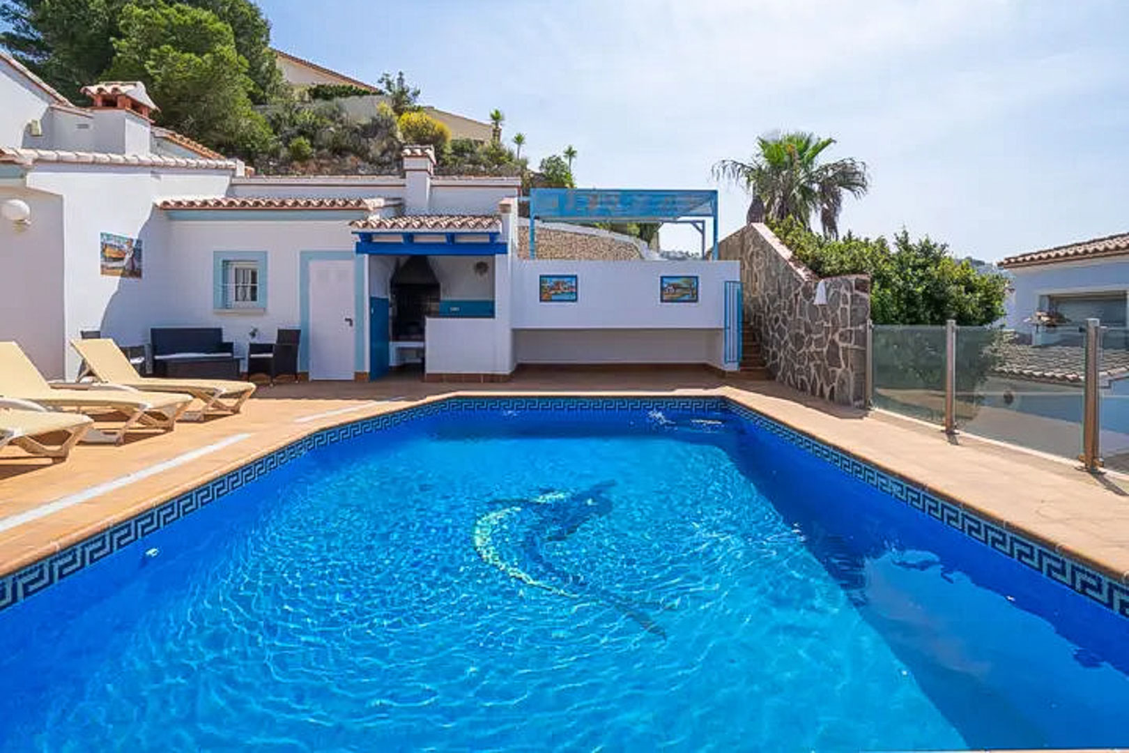 Außenpool mit Delfin-Mosaik und griechischem Muster, umgeben von einer Sonnenterrasse mit Liegestühlen und einem integrierten Grillbereich im mediterranen Stil.