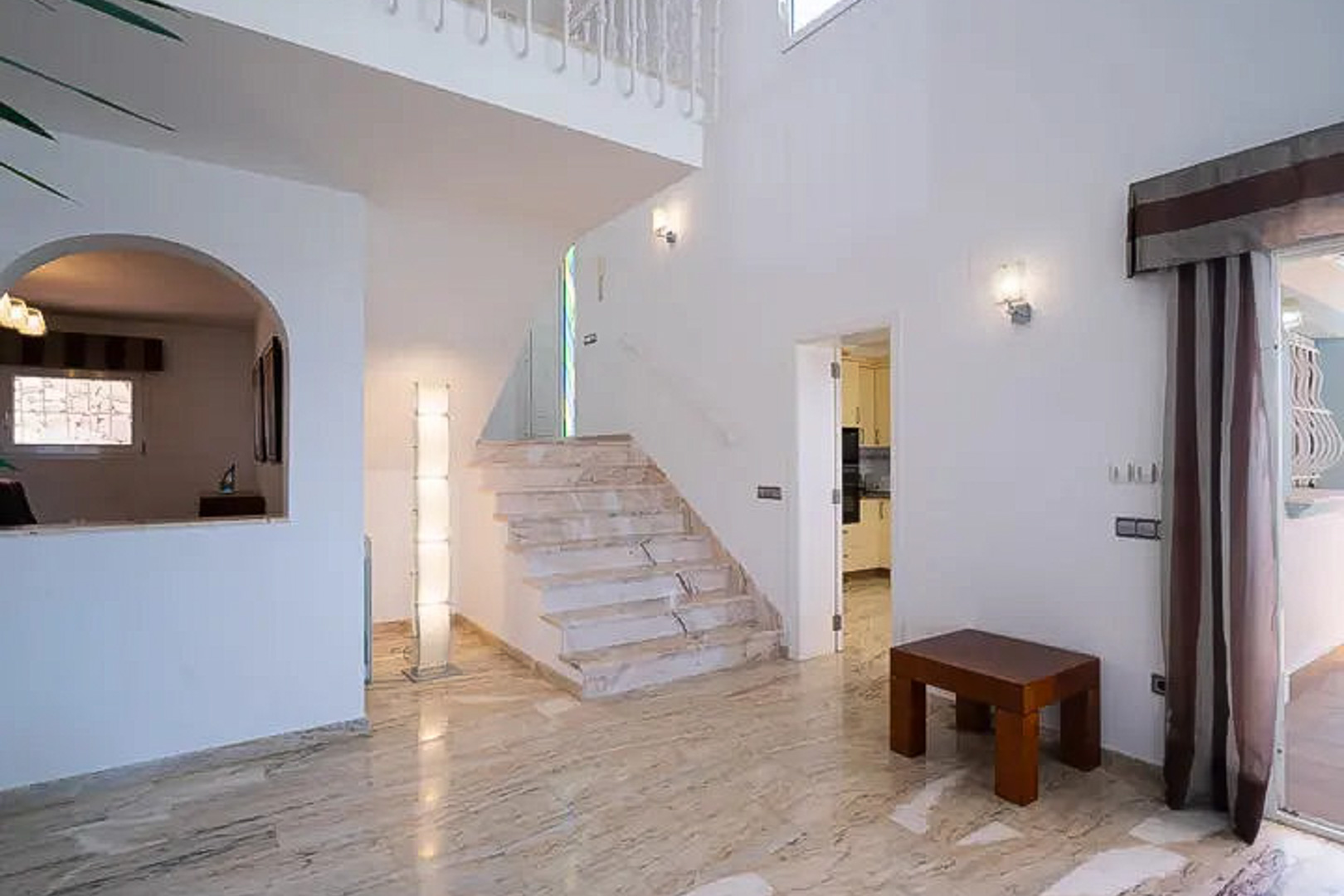 Eingangshalle mit polierten Marmorböden, einer eleganten Treppe und doppelter Deckenhöhe, die für viel natürliches Licht und Weite sorgt.