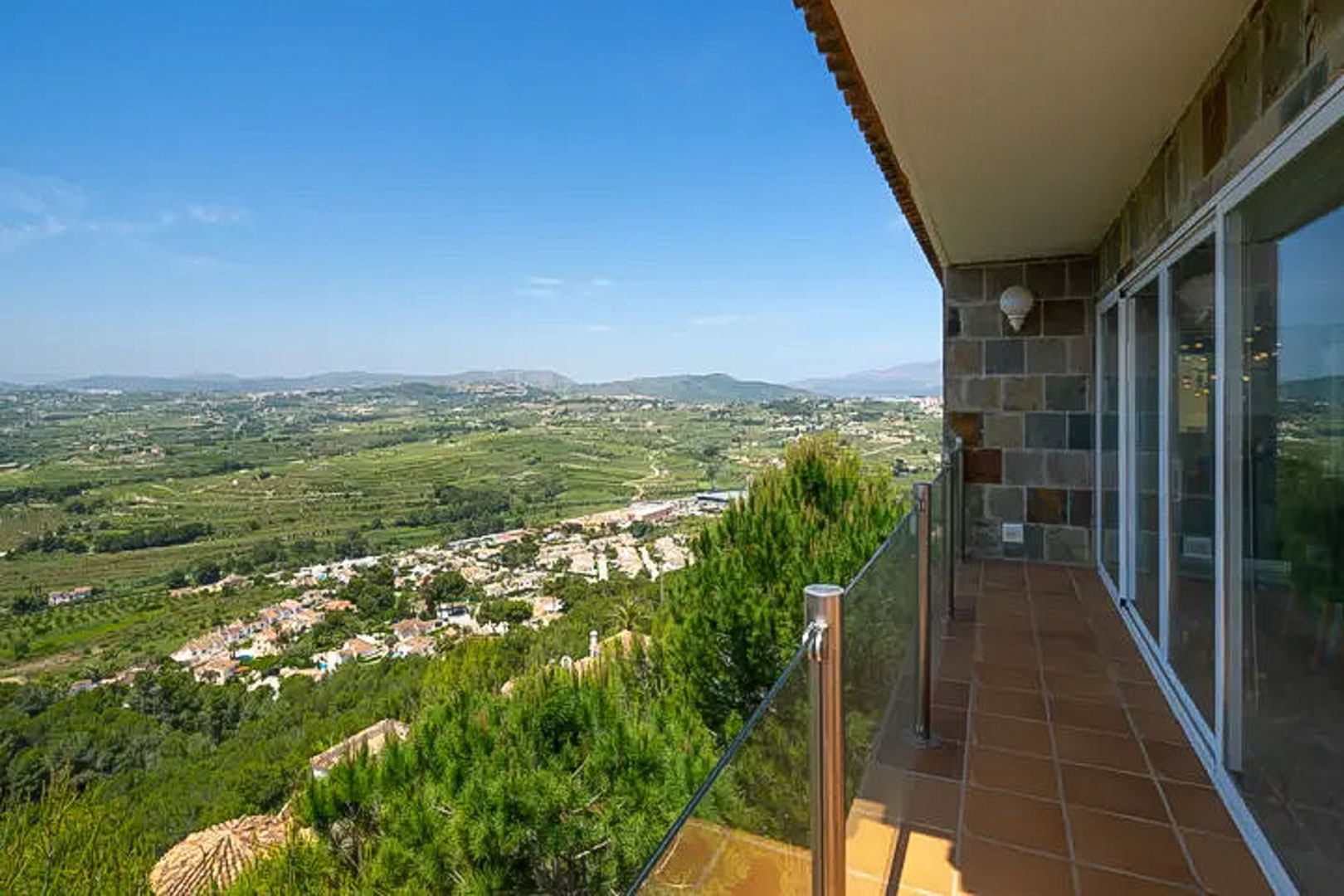 Hochgelegene Terrasse mit Terrakotta-Fliesen und Glasgeländer, die einen weiten Panoramablick über das Tal von Moraira und die Berge bietet.