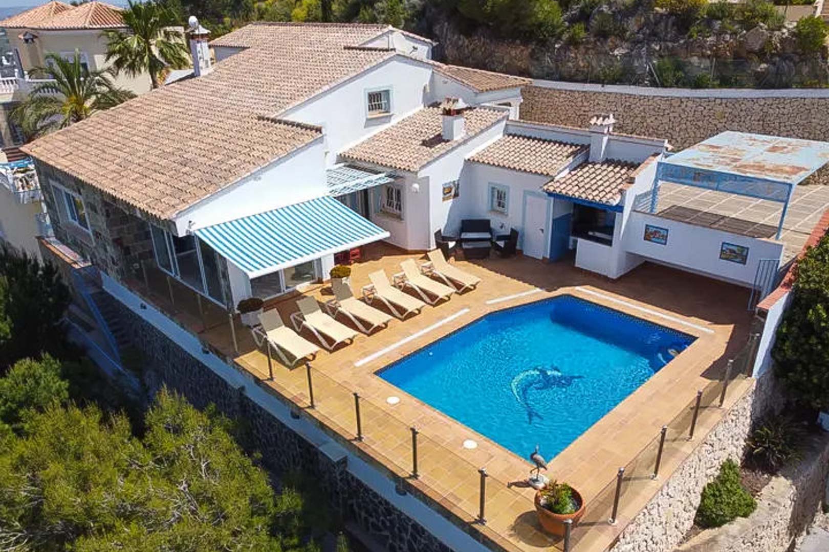 Luftbild der Villa mit privatem Pool, Sonnenterrasse mit Liegen, gestreifter Markise und Außenbar, eingefasst von modernen Glasgeländern.
