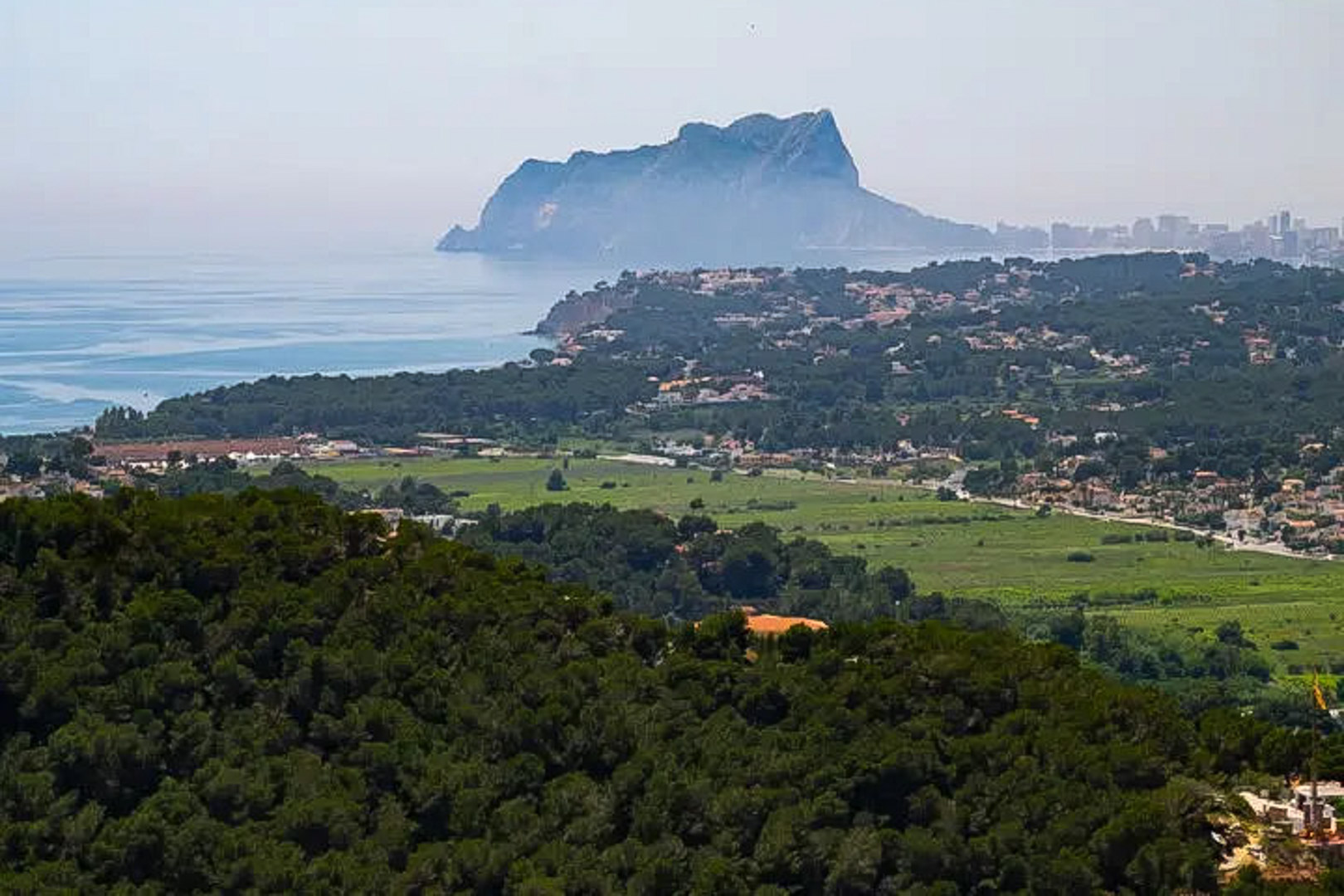 Panoramablick auf den Peñón de Ifach und die Küste, der den Kontrast zwischen dichten Pinienwäldern und dem Blau des Mittelmeers hervorhebt.