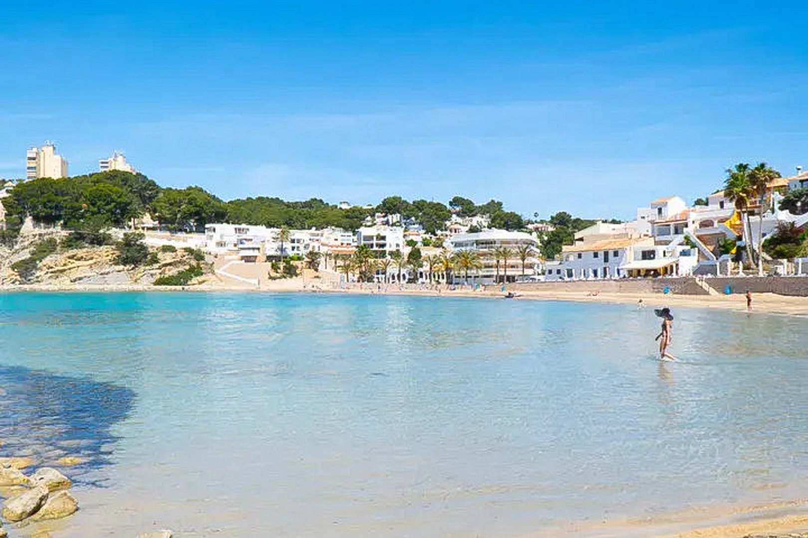 Panoramablick auf den Strand El Portet in Moraira mit flachem, türkisfarbenem Wasser und traditioneller weißer Architektur entlang der Küste.