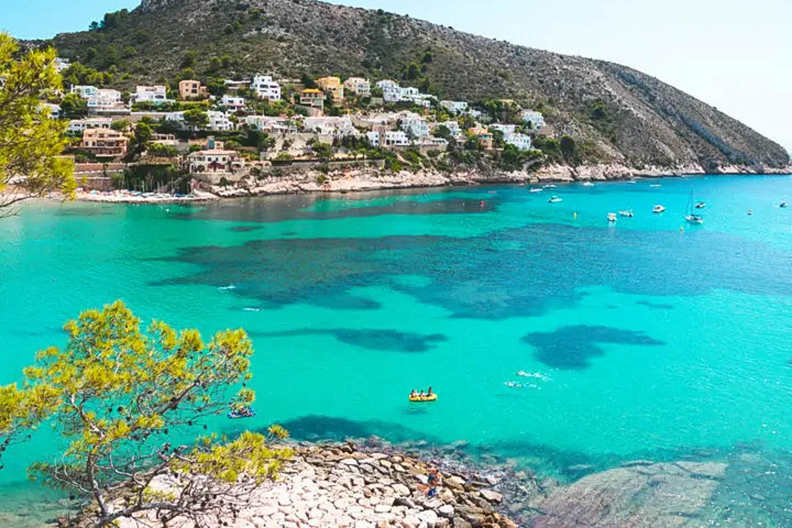Panoramablick auf eine Bucht in Moraira mit türkisfarbenem Wasser, Pinien und weißen Villen, die sich harmonisch in die felsige Küstenlandschaft einfügen.