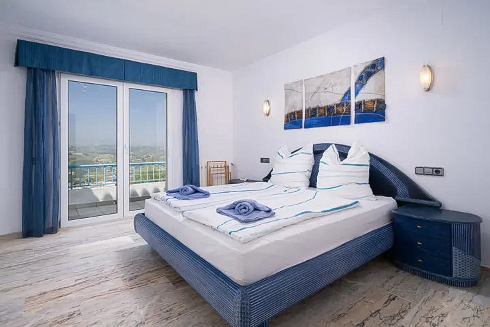 Schlafzimmer mit Marmorboden, Doppelbett in Blautönen und direktem Zugang zum Balkon mit weitem Blick über die Landschaft von Moraira.