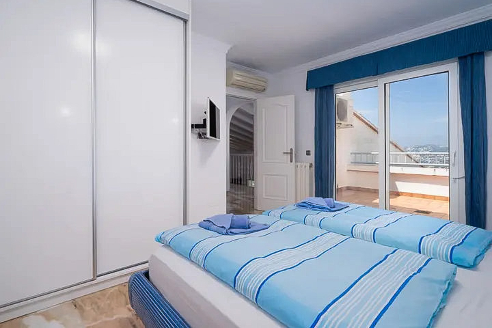 Schlafzimmer mit zwei Einzelbetten, großem weißen Schiebetürschrank und Zugang zur privaten Terrasse. Ausgestattet mit Klimaanlage, Wand-TV und Fliesenboden.