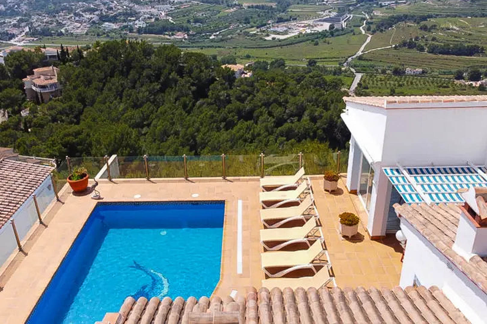 Terrasse mit rechteckigem Pool und Delfinmosaik, Sonnenliegen und Glasgeländer mit weitem Blick über das Tal und die Berge von Moraira.