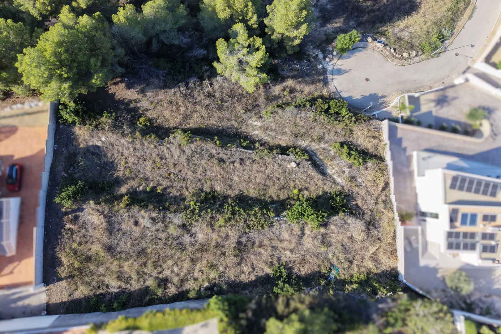 Luftaufnahme des terrassierten Baugrundstücks mit Natursteinmauern, umgeben von Pinien und gelegen an einer ruhigen Sackgasse in Moraira.