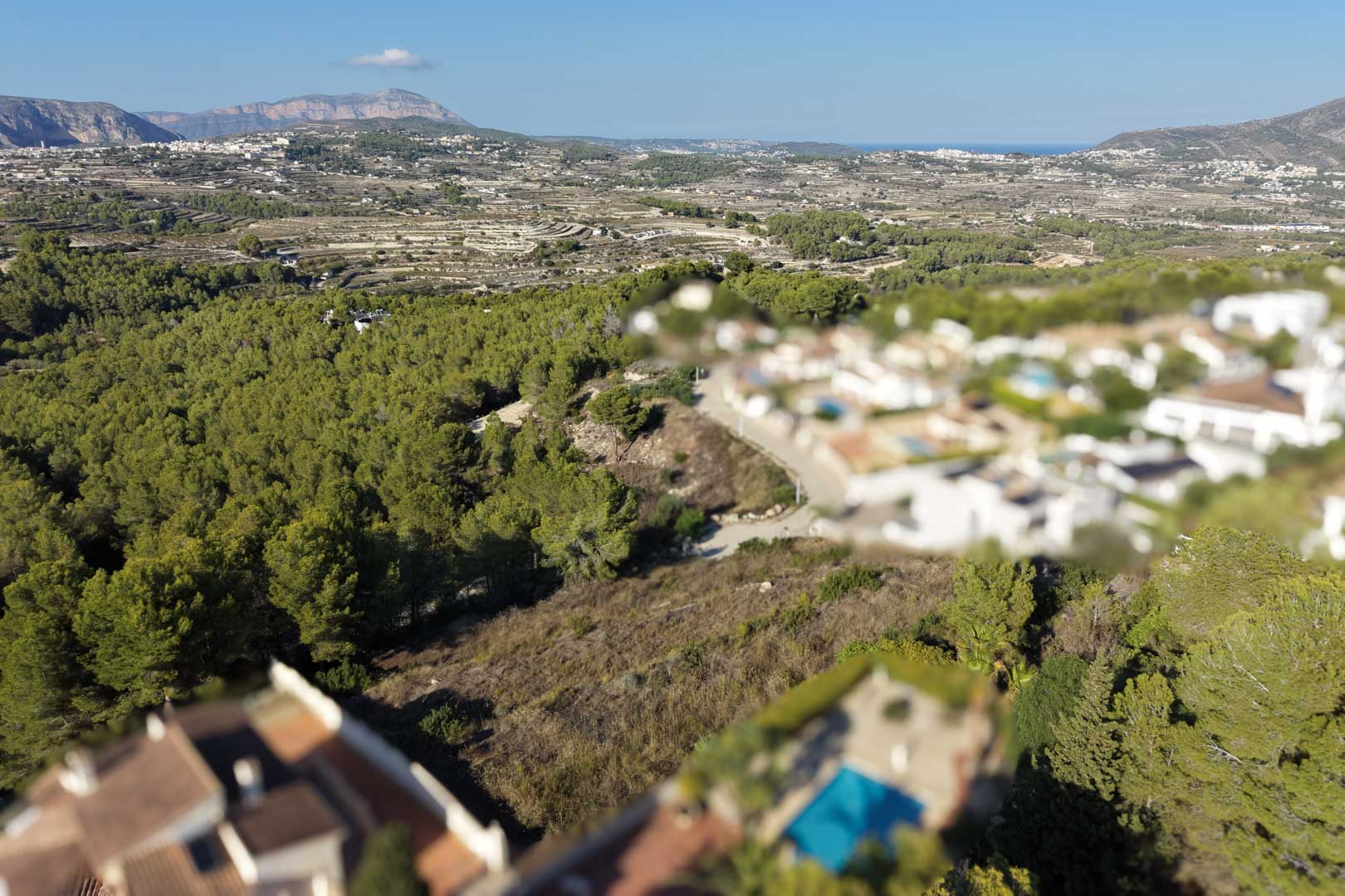 Erhöhte Luftaufnahme des Baugrundstücks mit mediterraner Vegetation und weitem Blick über das Tal von Moraira bis hin zum Meer.